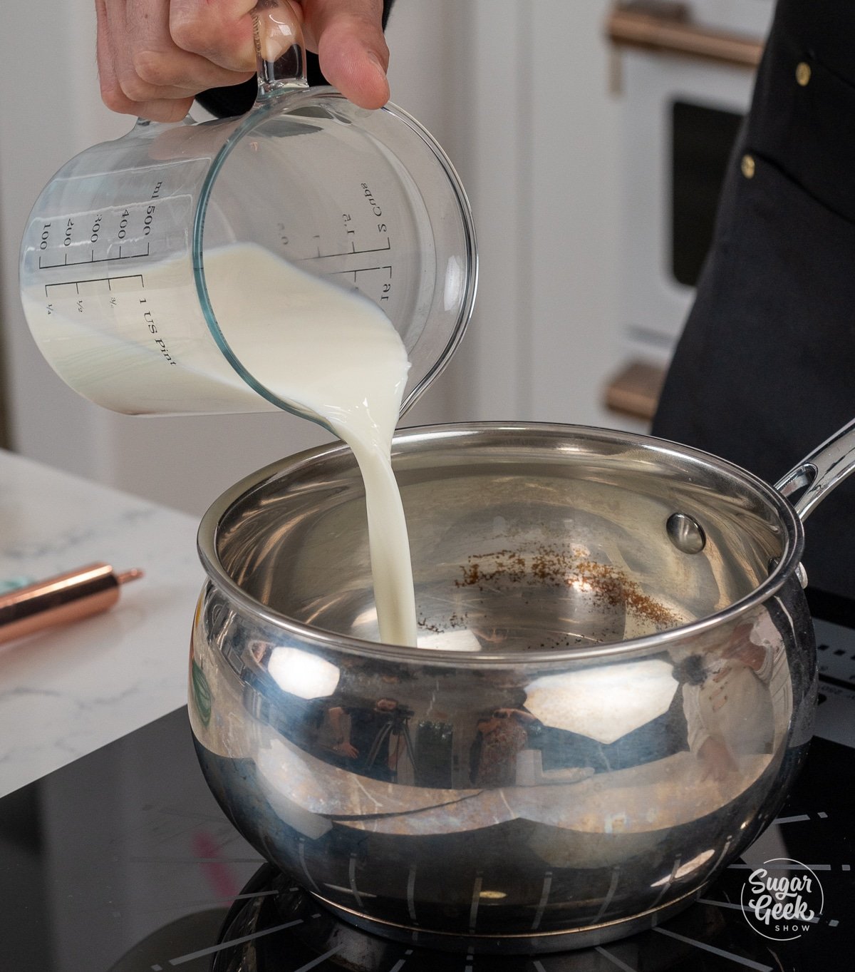 hand adding container of milk into a metal saucepan