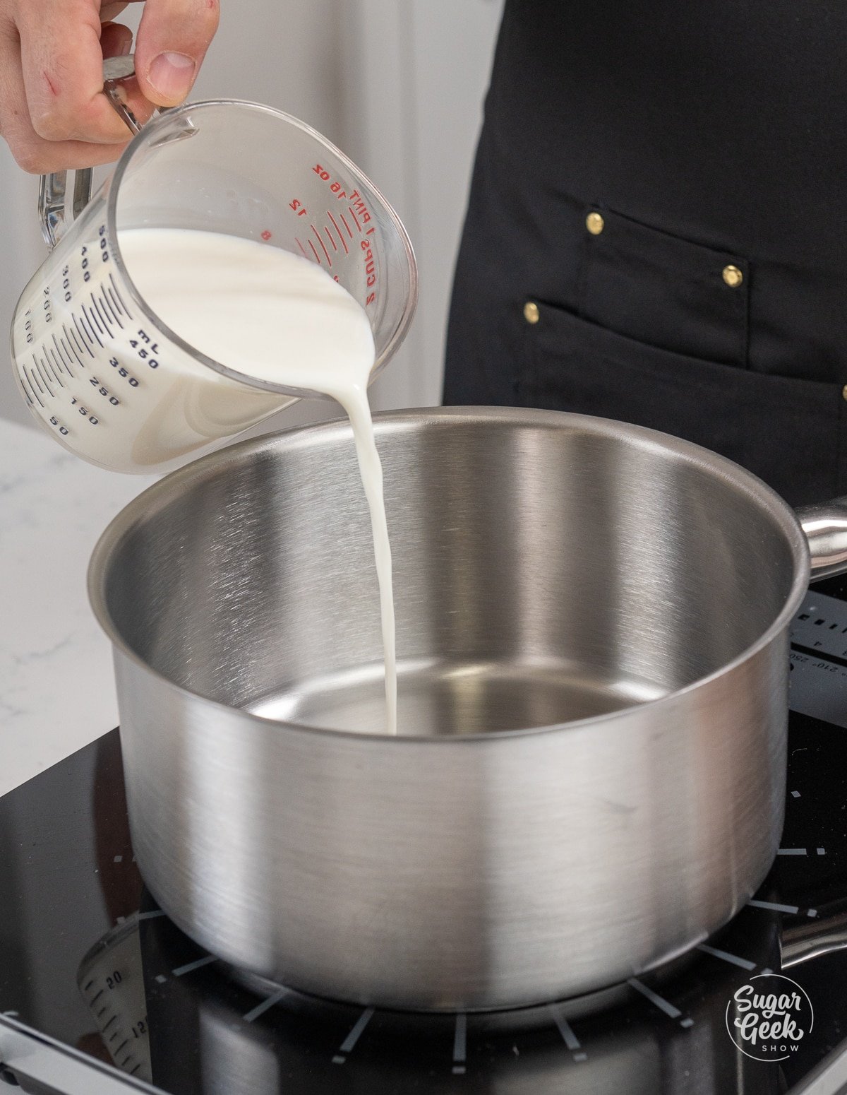 hand adding a container of milk to a metal saucepan