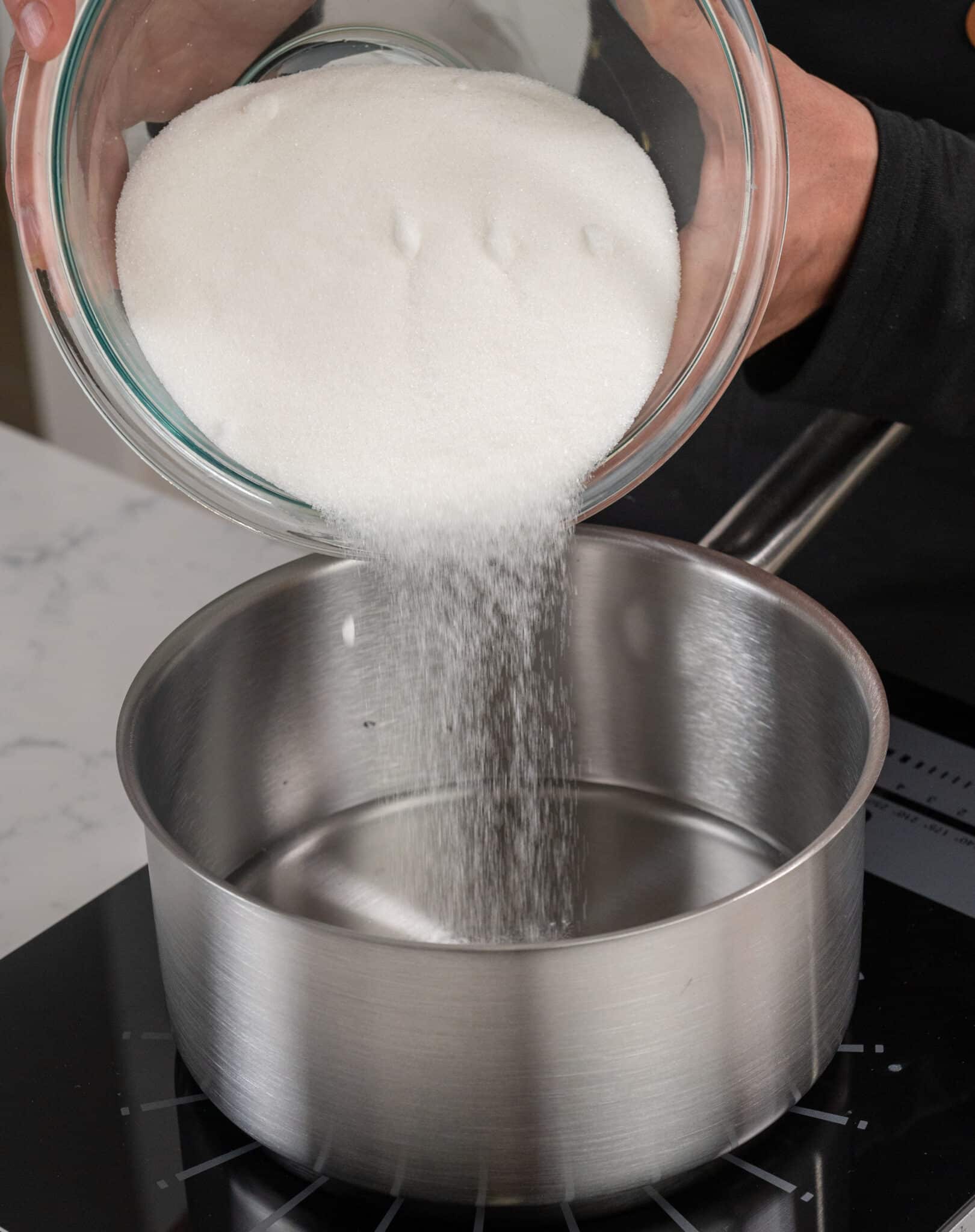 hands pouring a bowl of sugar into a large metal saucepan