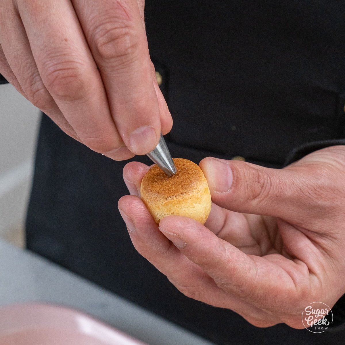 hand pressing a small hole into the bottom of a cream puff with a piping tip.