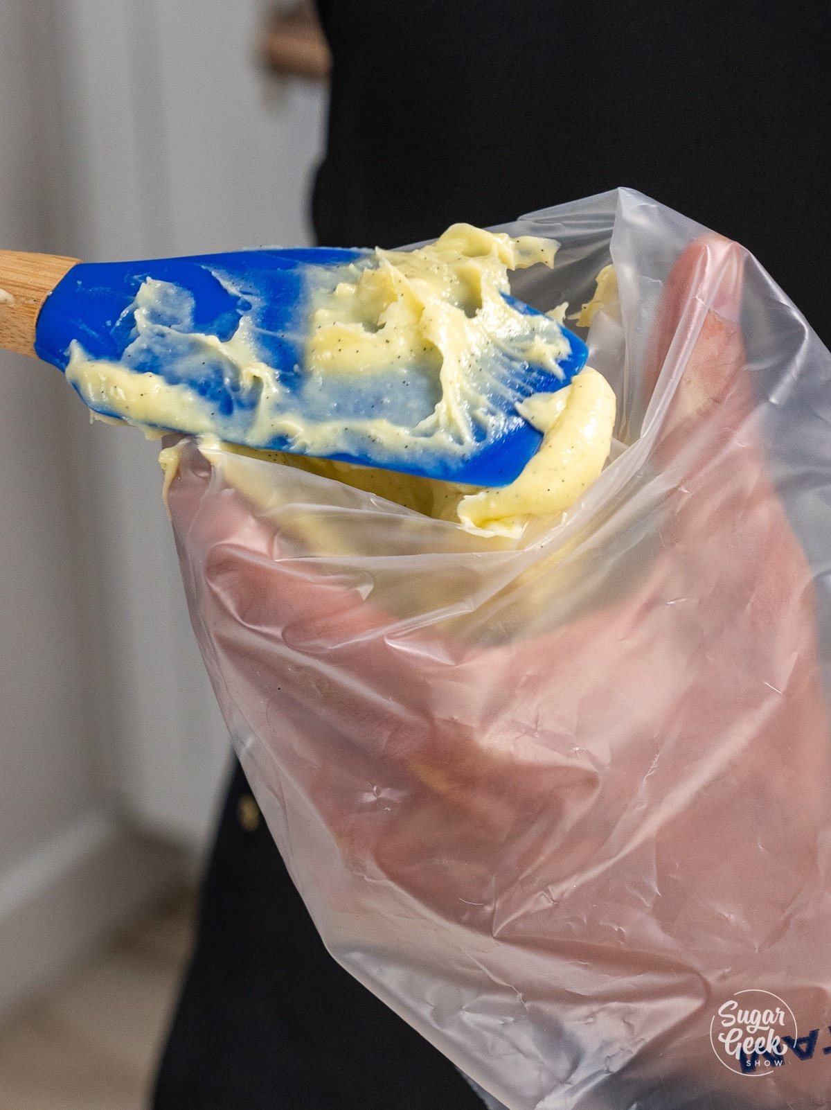 hand holding a pastry bag while a spatula fills it with pastry cream.