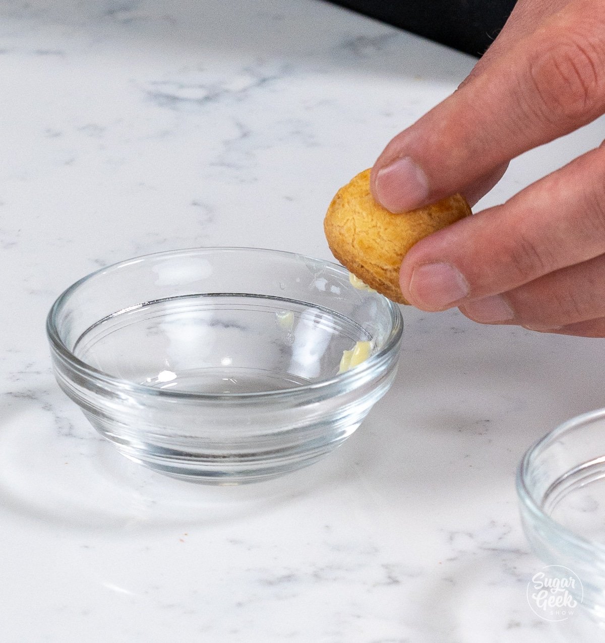 hand scraping a cream puff against the side of a small bowl to remove excess filling.