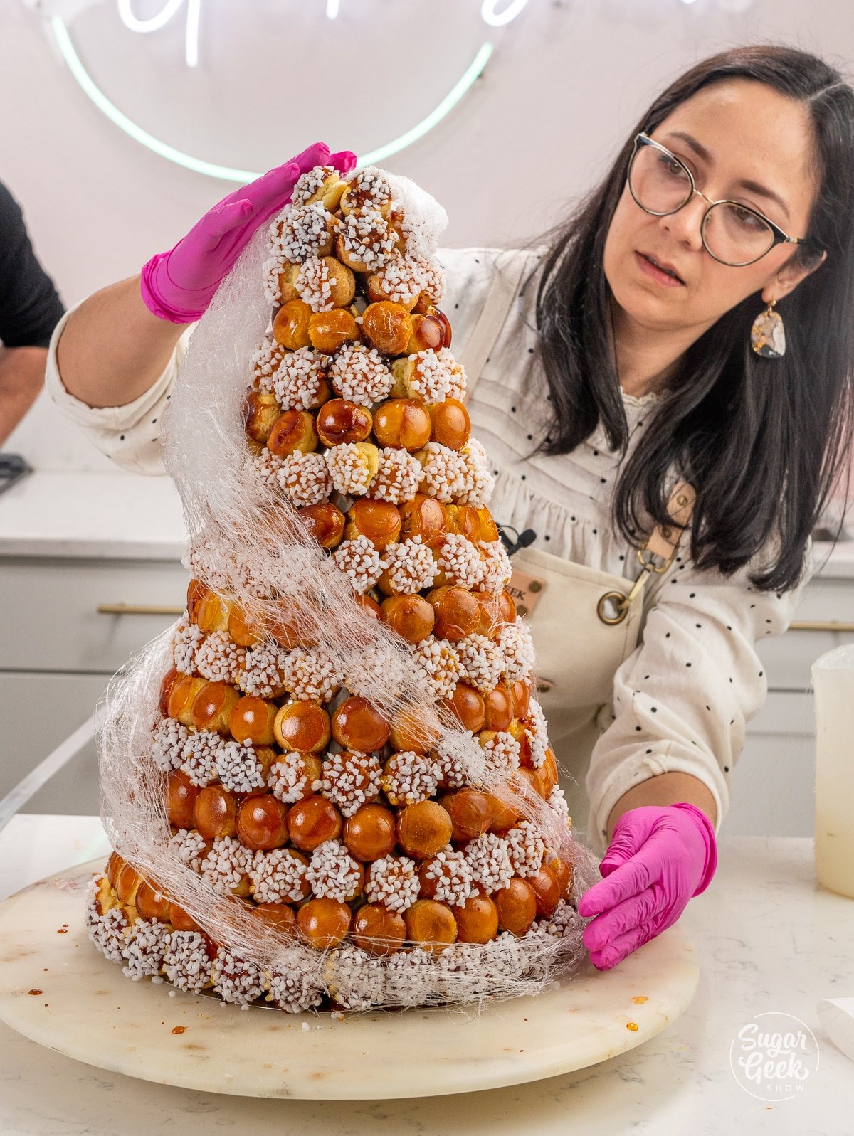 woman wearing pink gloves using hands to assemble a croquembouche