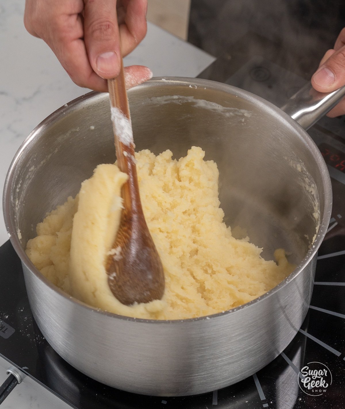 wooden spoon stirring choux dough in a metal pot