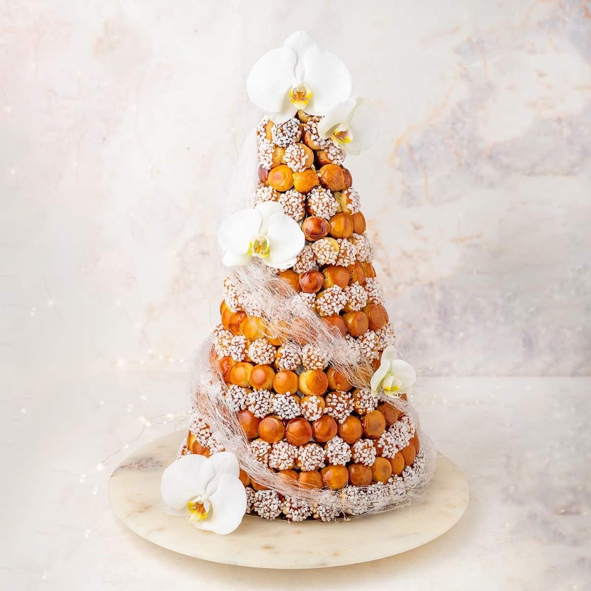 wedding cream puff tower stacked on top of a marble plate in front of white background