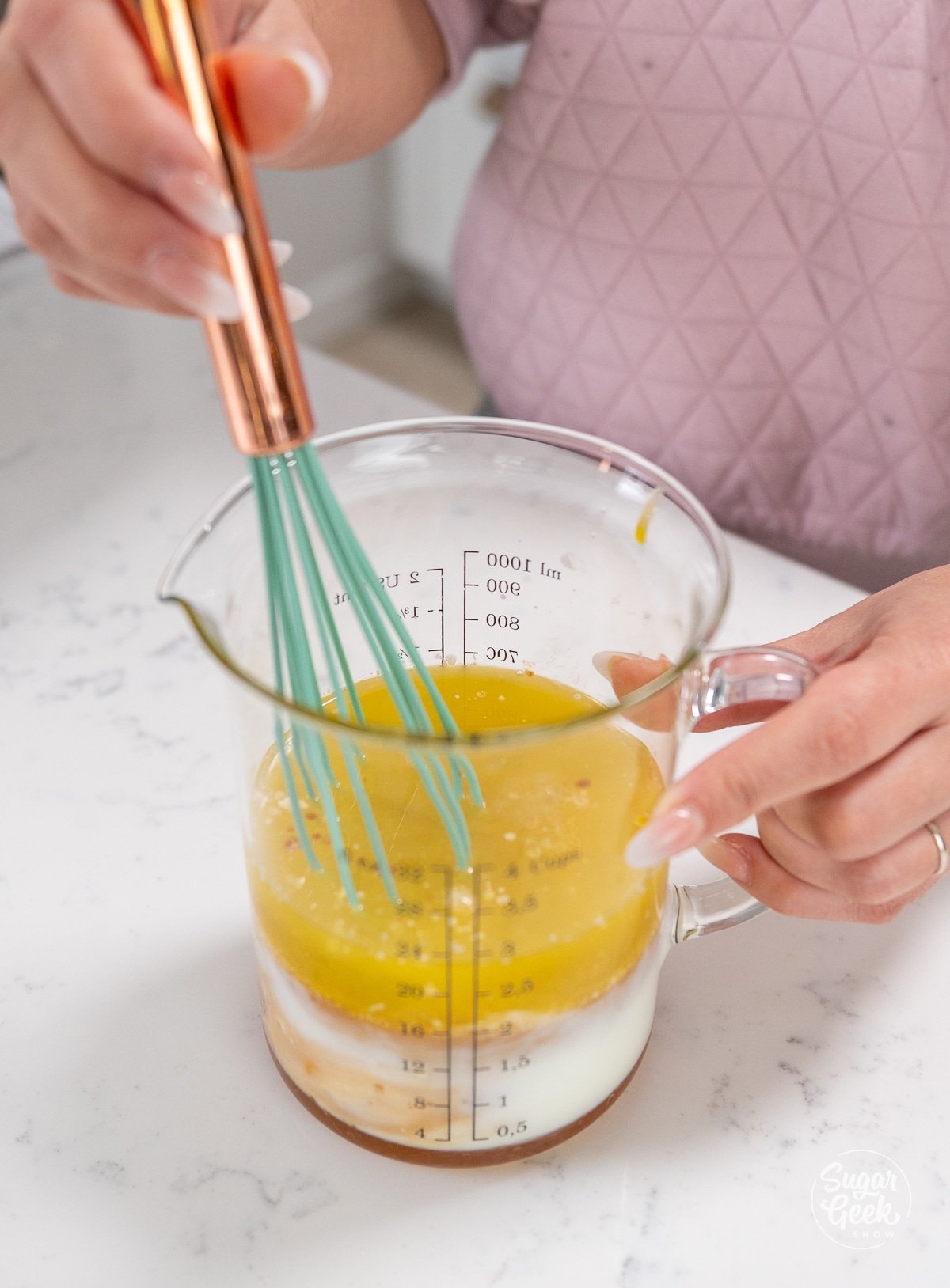 whisking honey cake wet ingredients in a large measuring cup.
