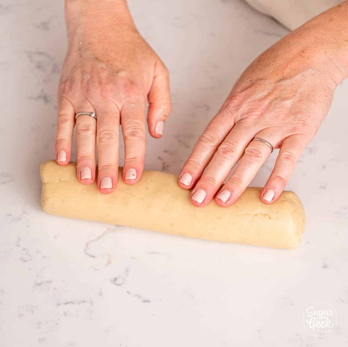 hands rolling marzipan into a log shape. 