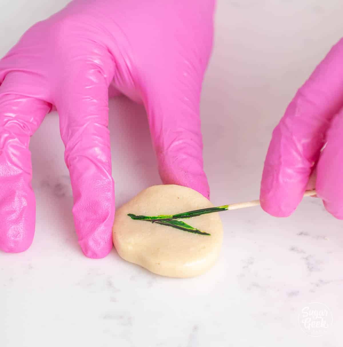 hands spreading green gel food color on marzipan with a toothpick.