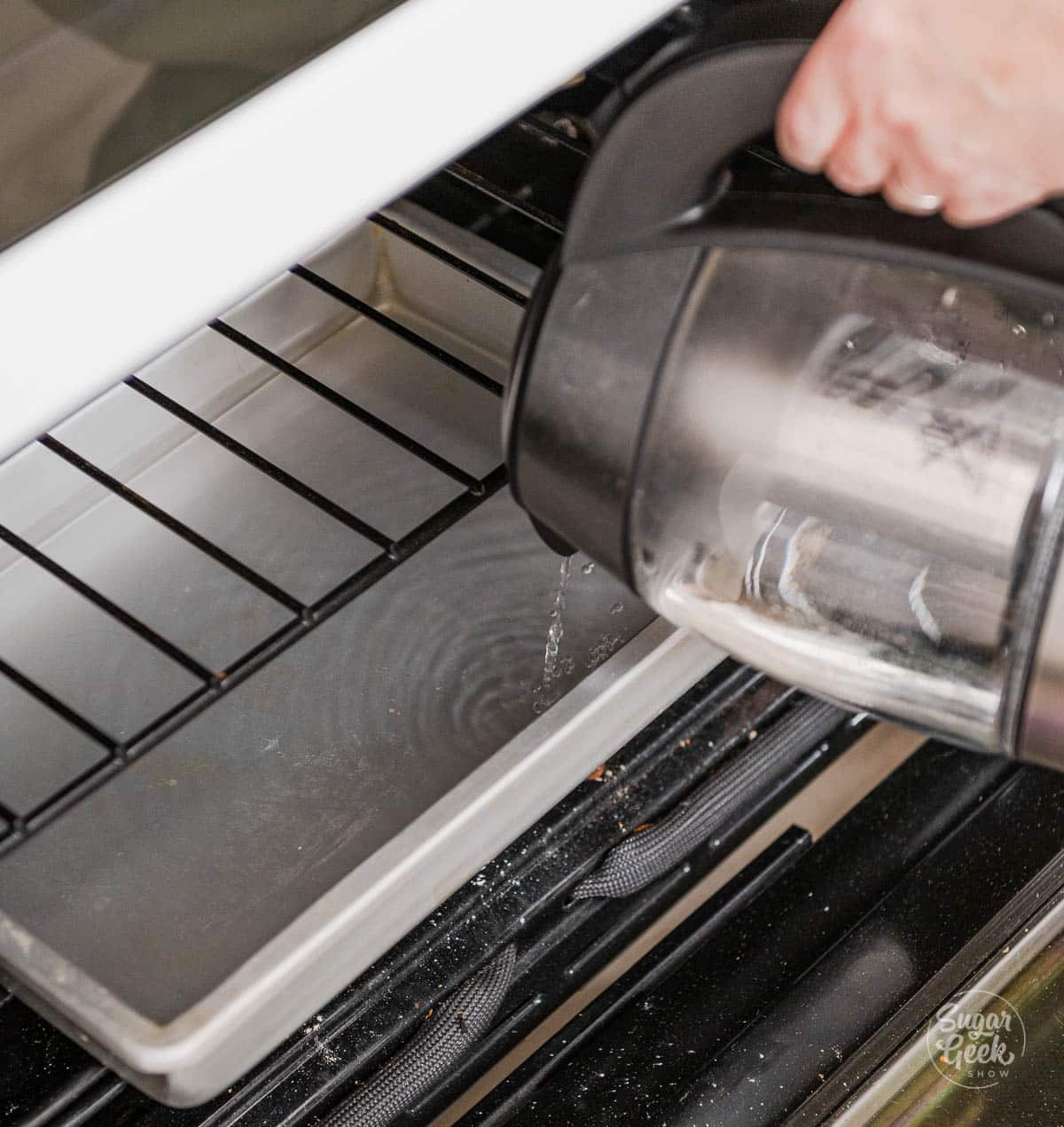 hand pouring boiling water out of a container to a sheet pan in the oven
