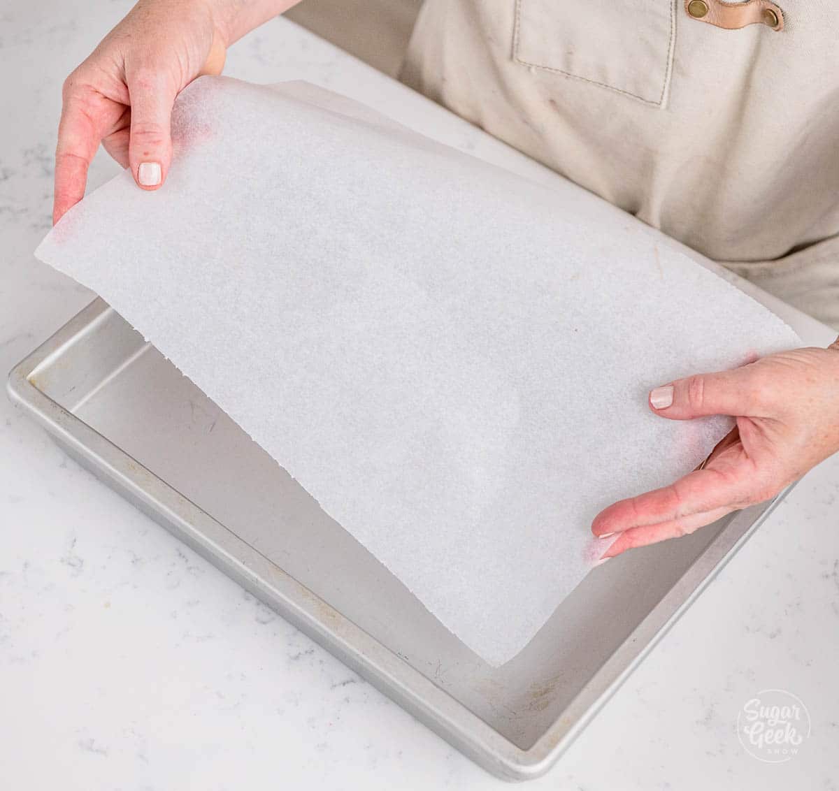hands placing a sheet of parchment paper into a 9x12 sheet pan