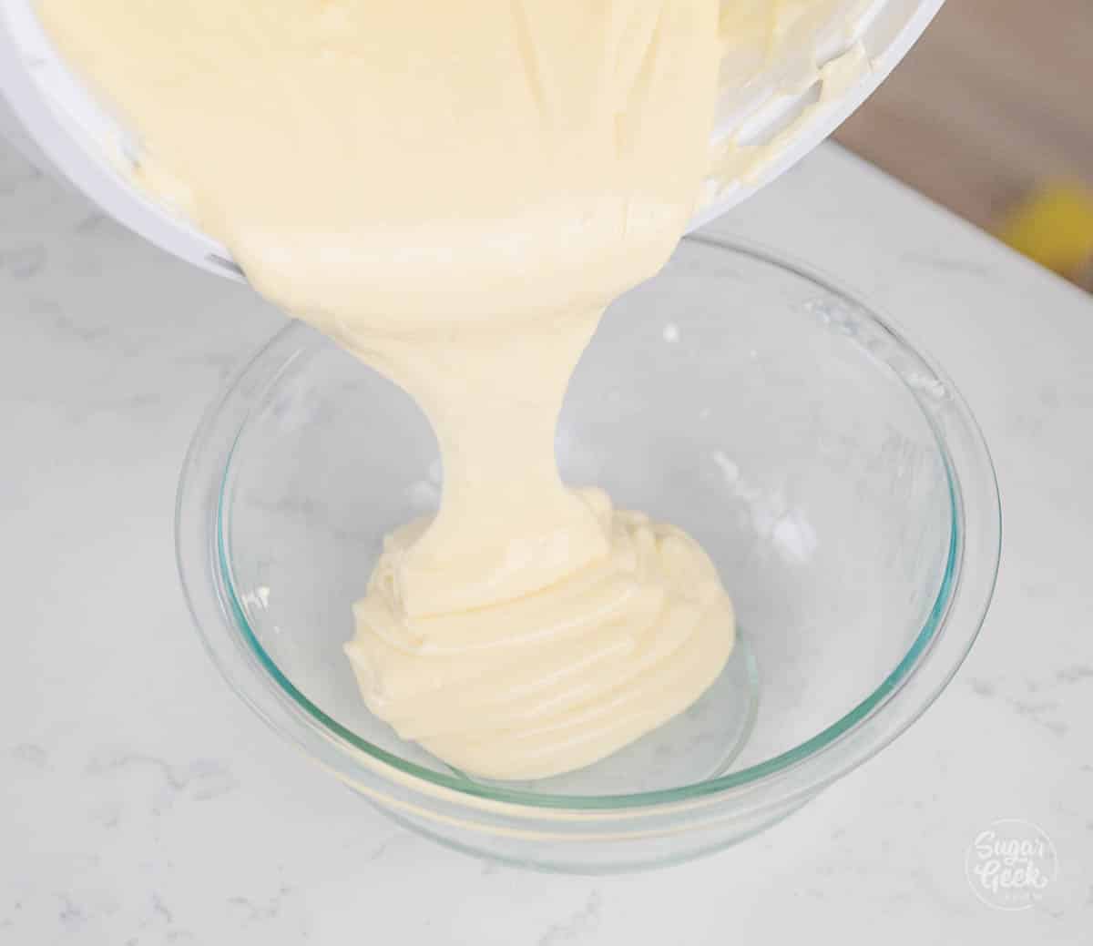 cheesecake batter pouring from a white bowl into a smaller clear bowl