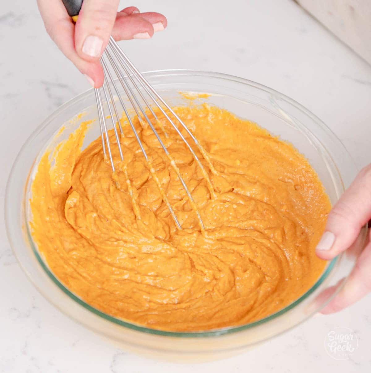hand holding a whisk mixing a bowl of pumpkin pie batter