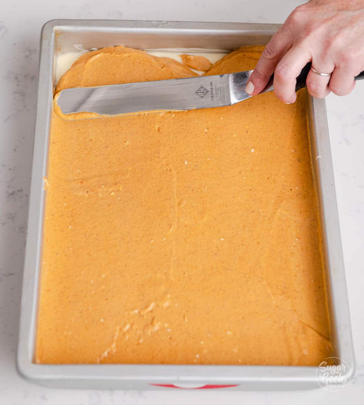 hand holding an offset spatula spreading pumpkin pie batter