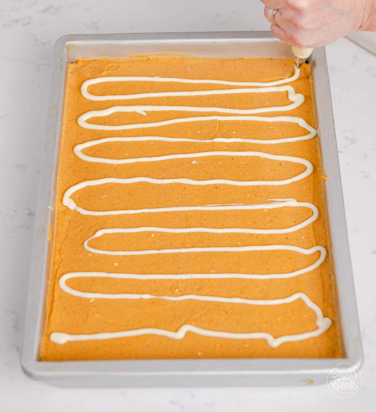 hand drawing horizontal white lines of cheesecake batter