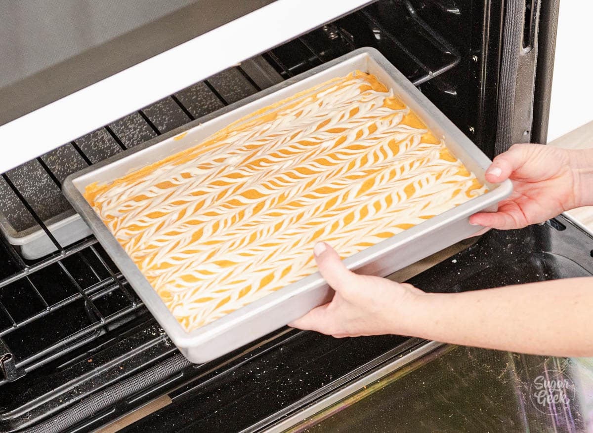 hands placing a baking pan with pumpkin cheesecake bars into the oven