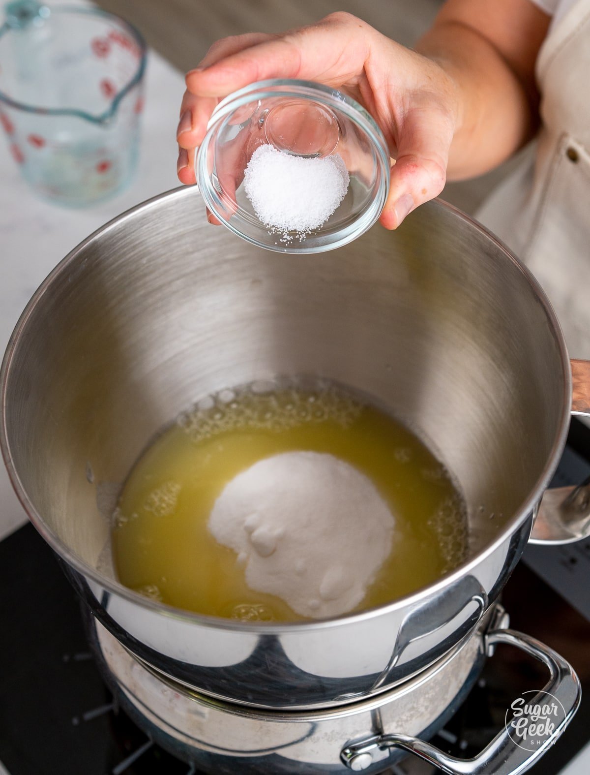 hand adding salt to stand mixer bowl with egg whites and sugar.