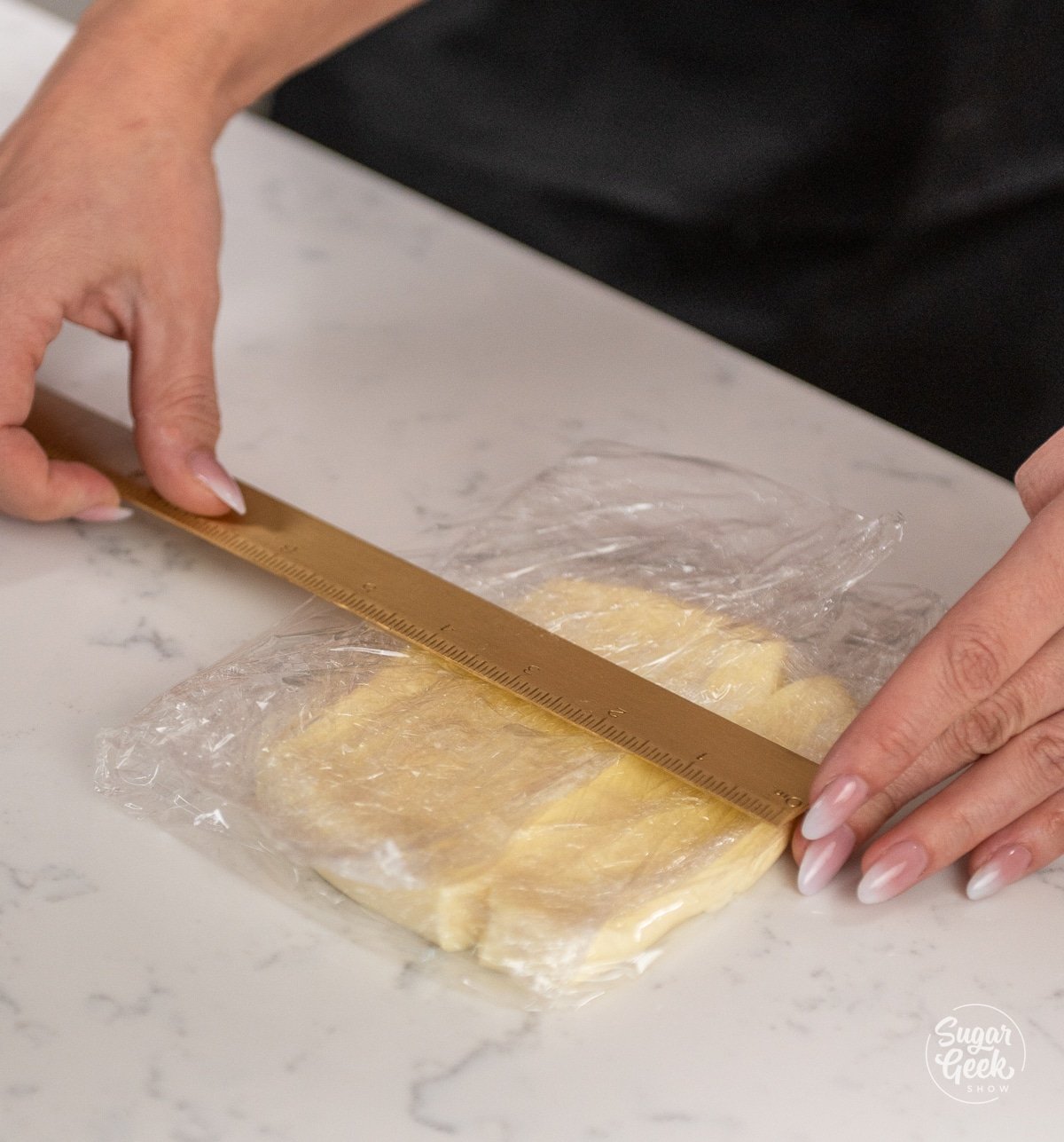 hands holding a ruler over a square piece of plastic wrap and butter