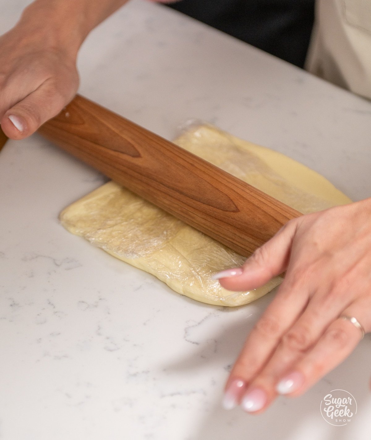 hands holding a wooden rolling pin over a butter block