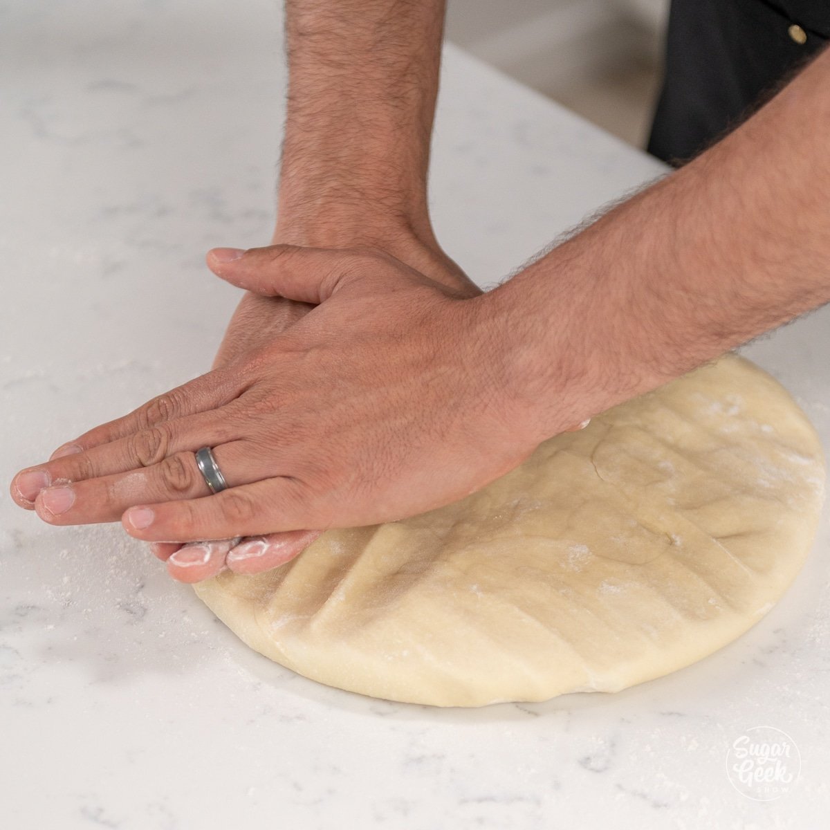two hands pressing down croissant dough in a large circle