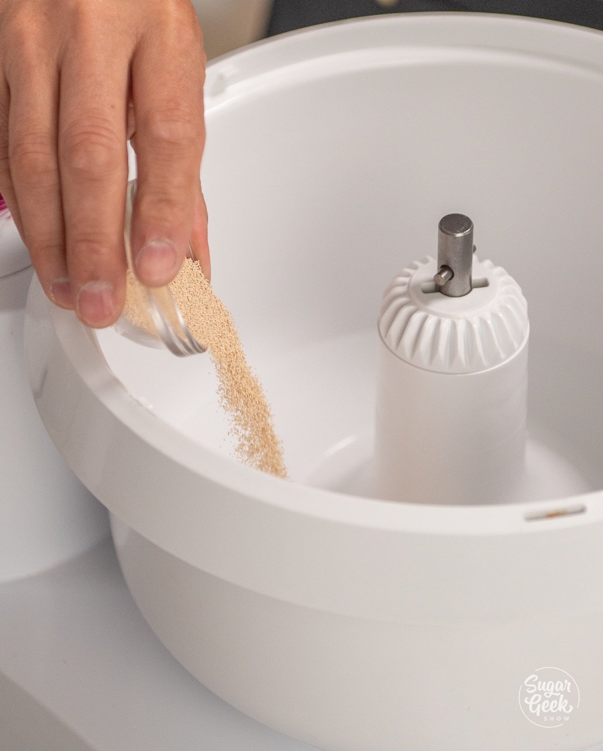 hand adding a bowl of yeast into a white stand mixer bowl