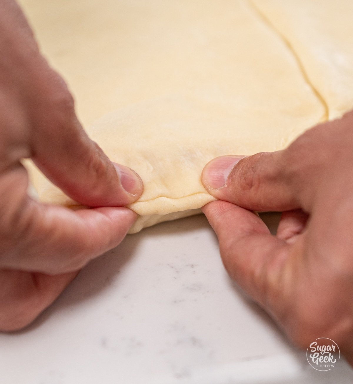two hands pinching the edge of a block of croissant dough and butter