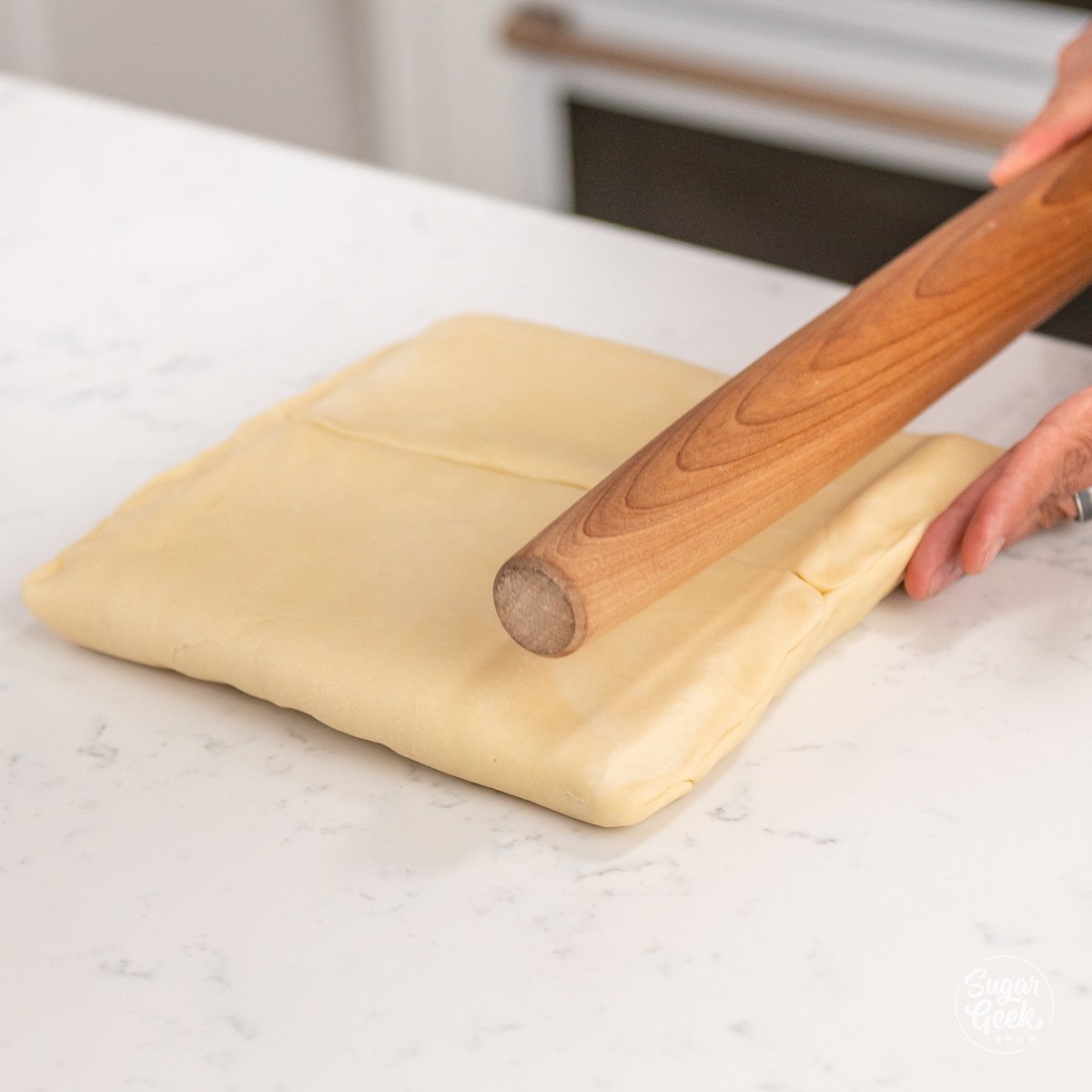 wooden rolling pin on top of a block of croissant dough and butter