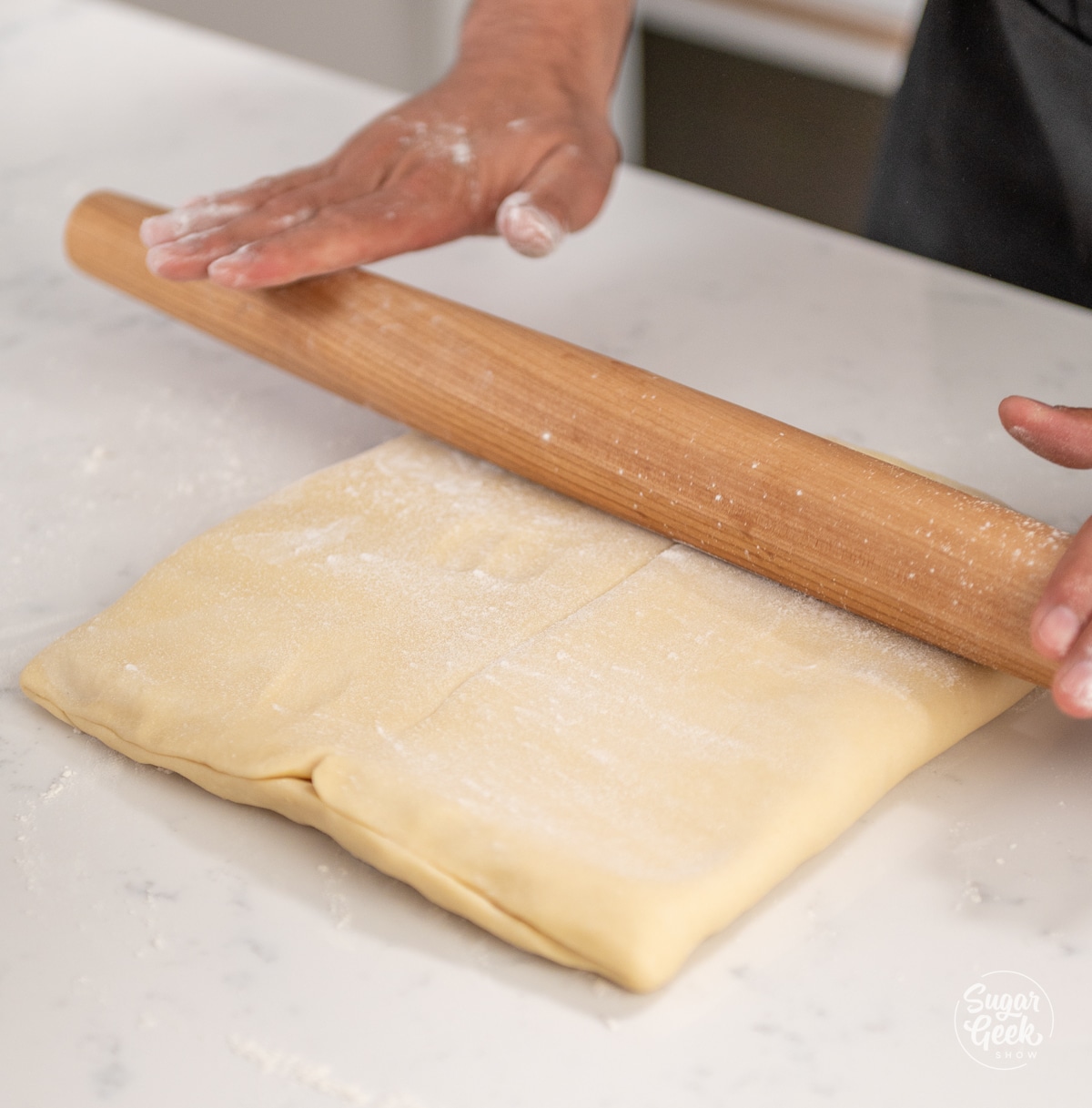 hands holding a rolling pin on top of croissant dough