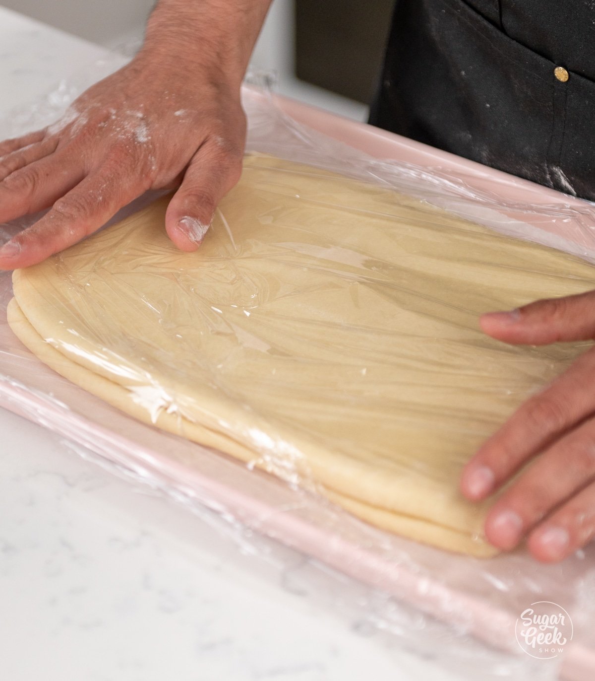 hands placing plastic wrap over the top of croissant dough on a baking sheet