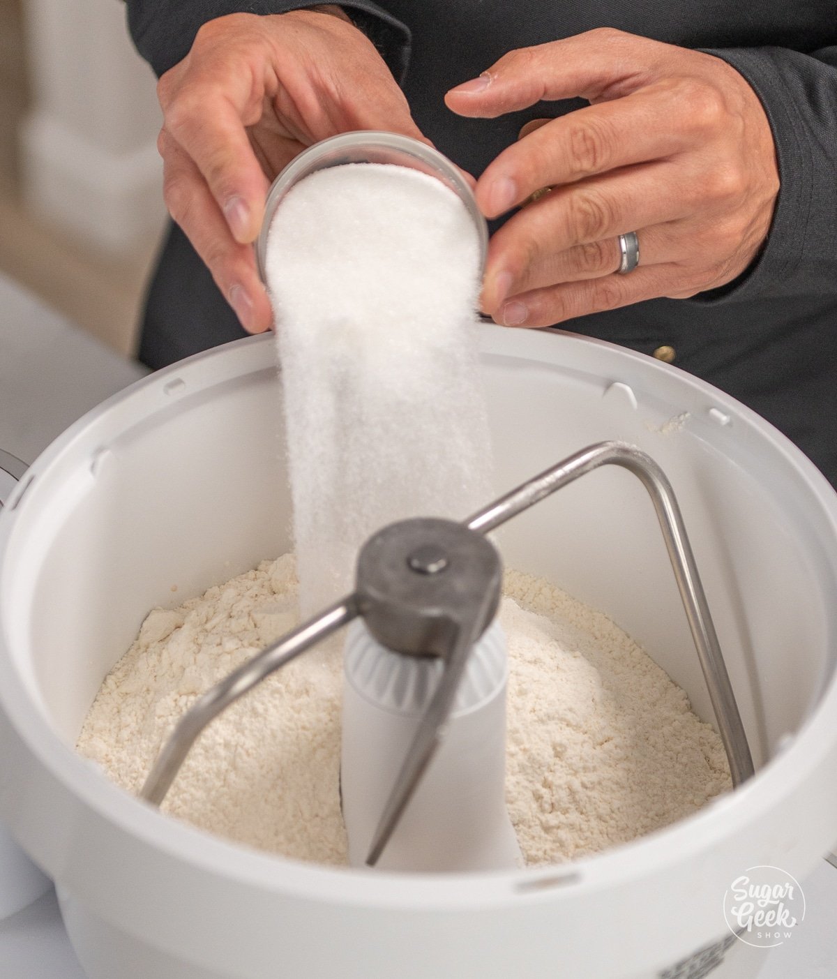 hand adding a bowl of sugar into a white stand mixer bowl