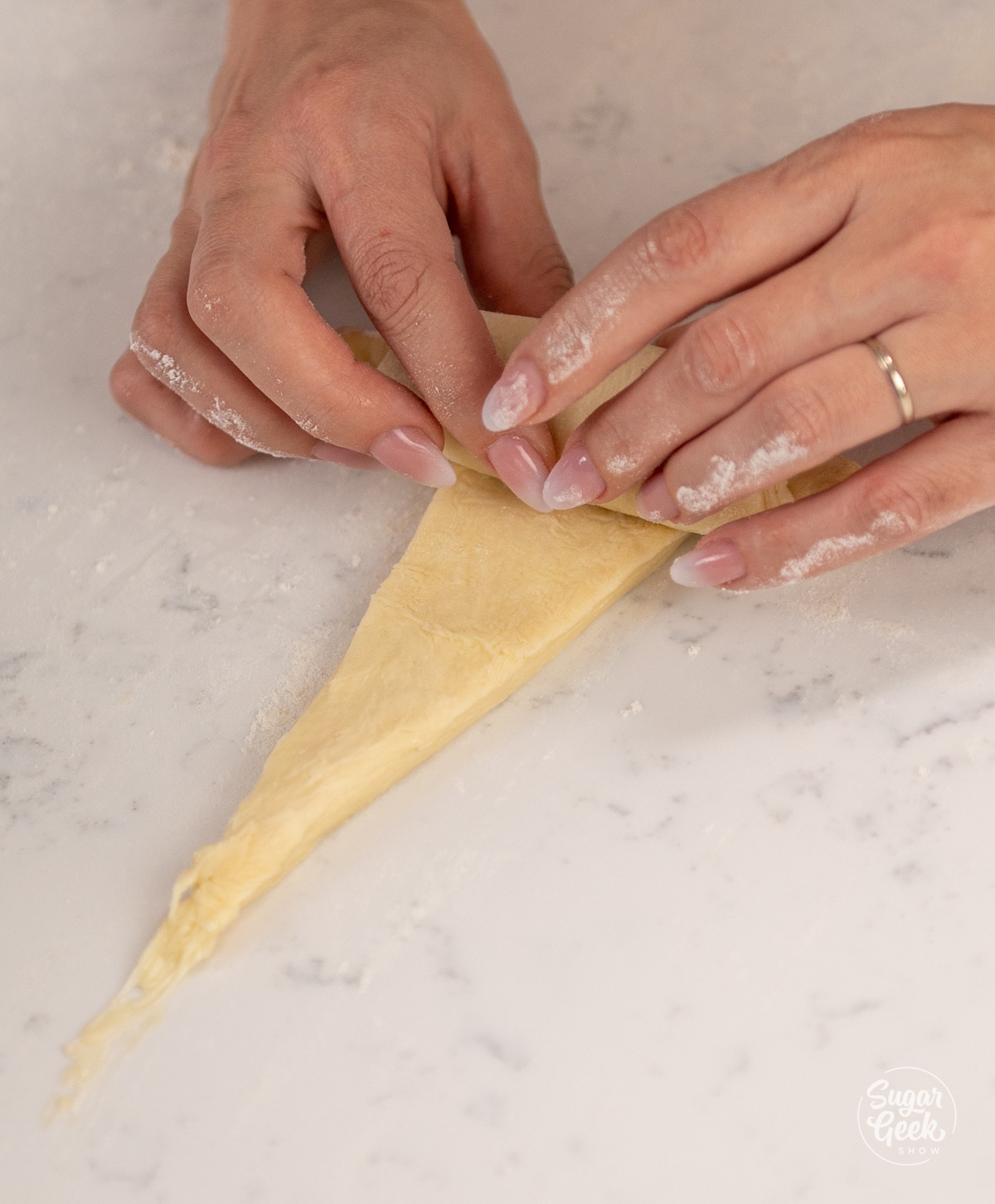 two hands rolling a triangle of dough