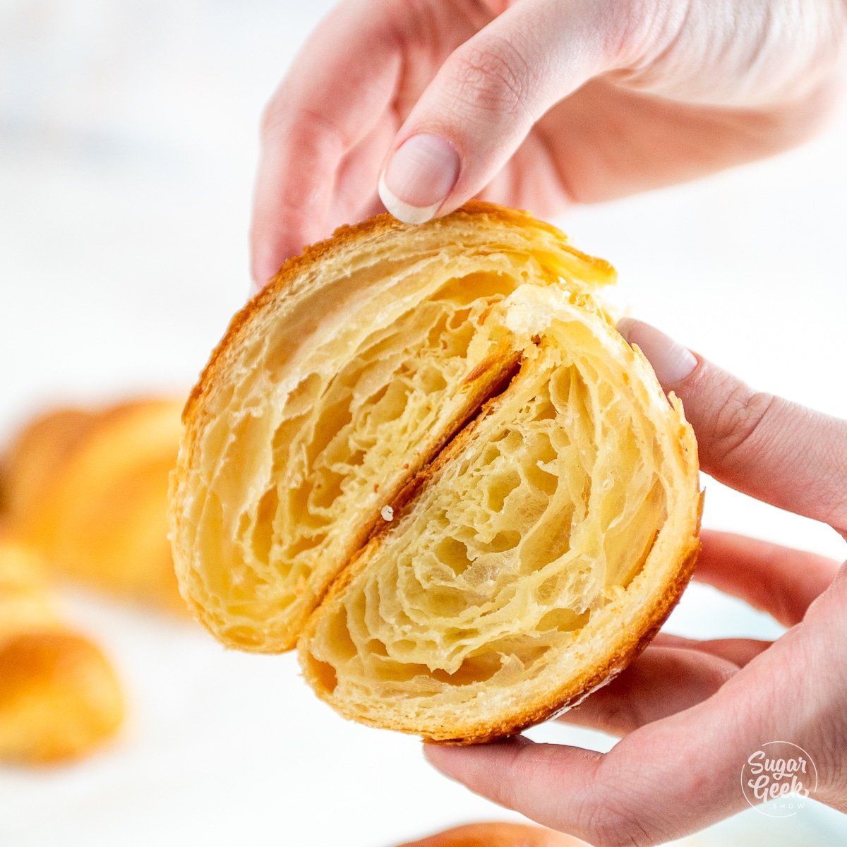 hands holding open a croissant to show the flaky inside layers