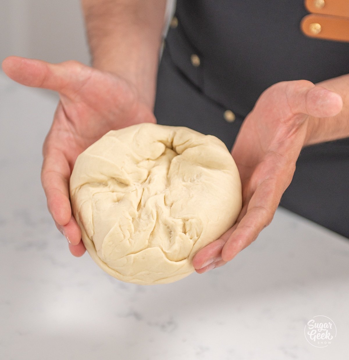 hands holding a ball of croissant dough with the rough edges up
