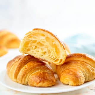 half open croissant laying on top of two other croissants on a plate