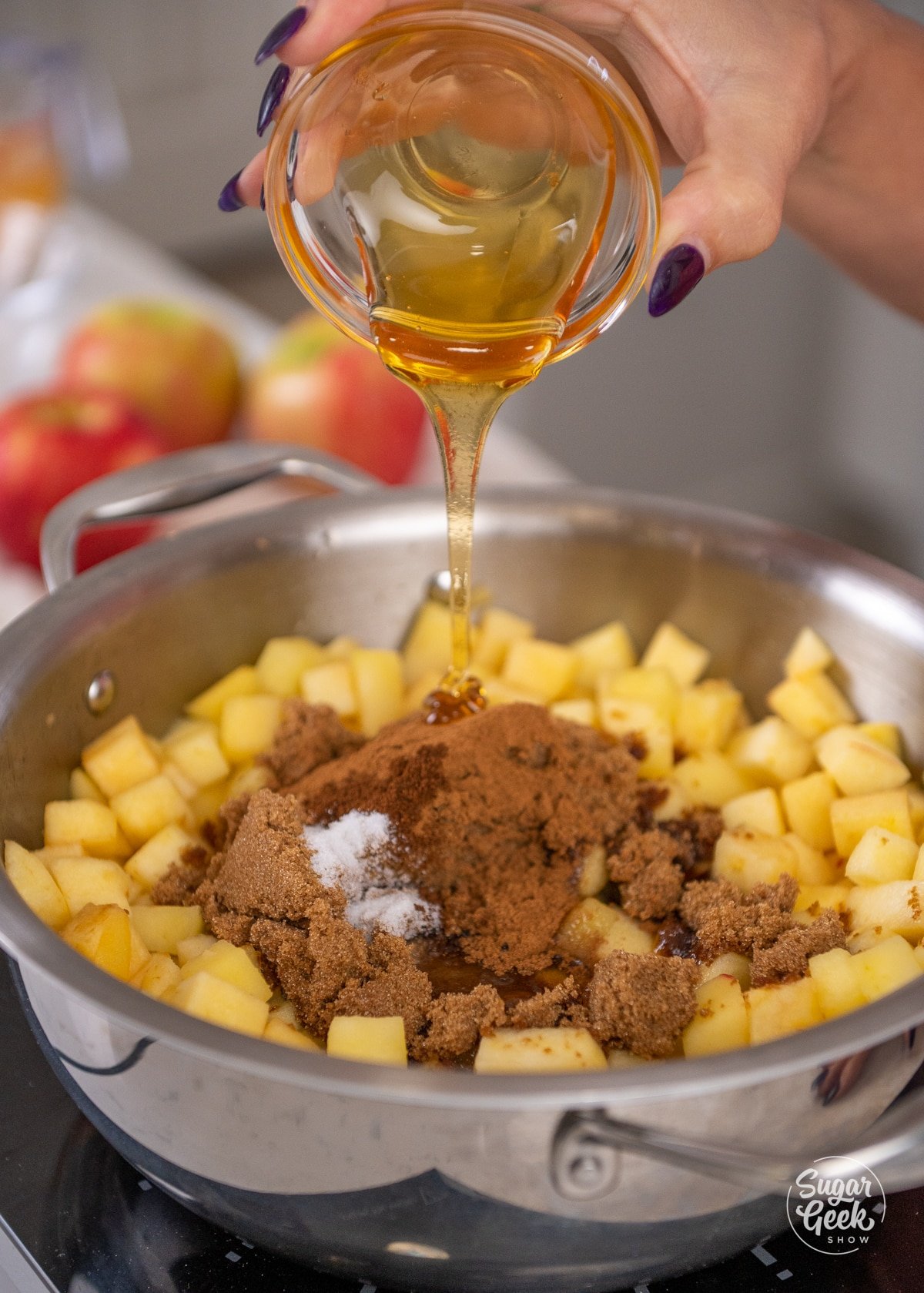 hand adding honey to apples with sugar and spices in a saucepan.