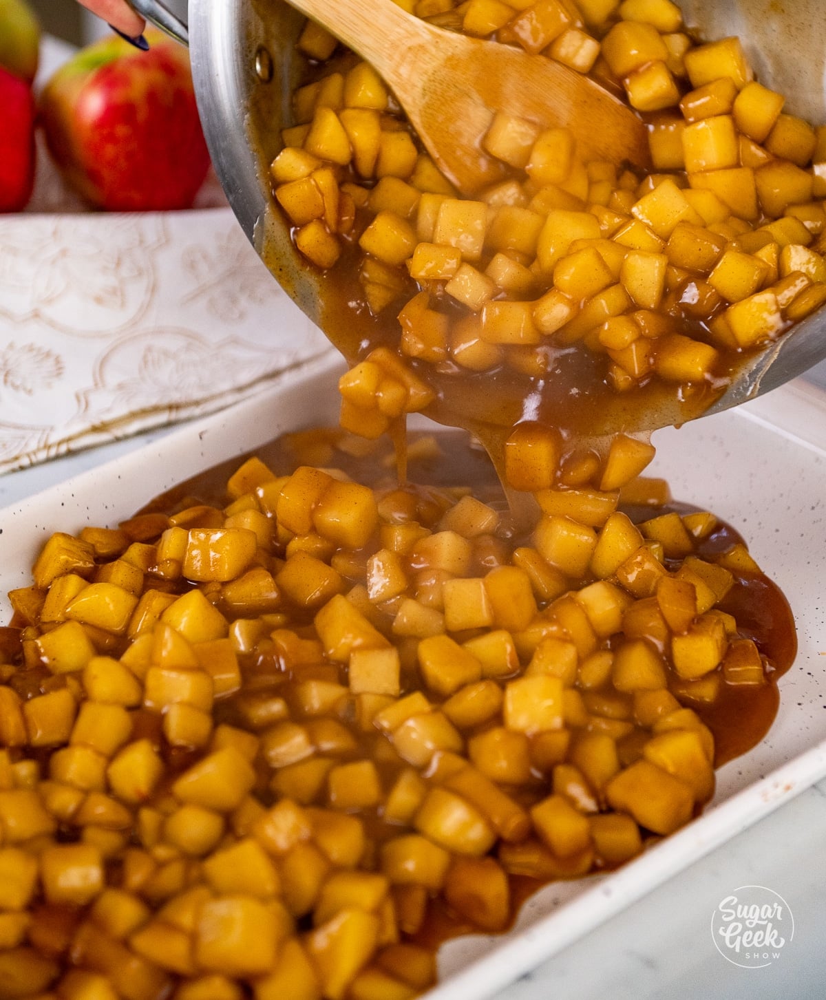 Pouring warm apple filling from the pan into a shallow white baking dish to cool