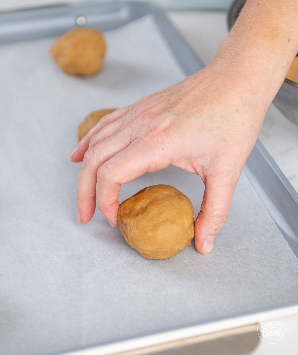 hand placing a ball of peanut butter cookie dough onto a baking sheet