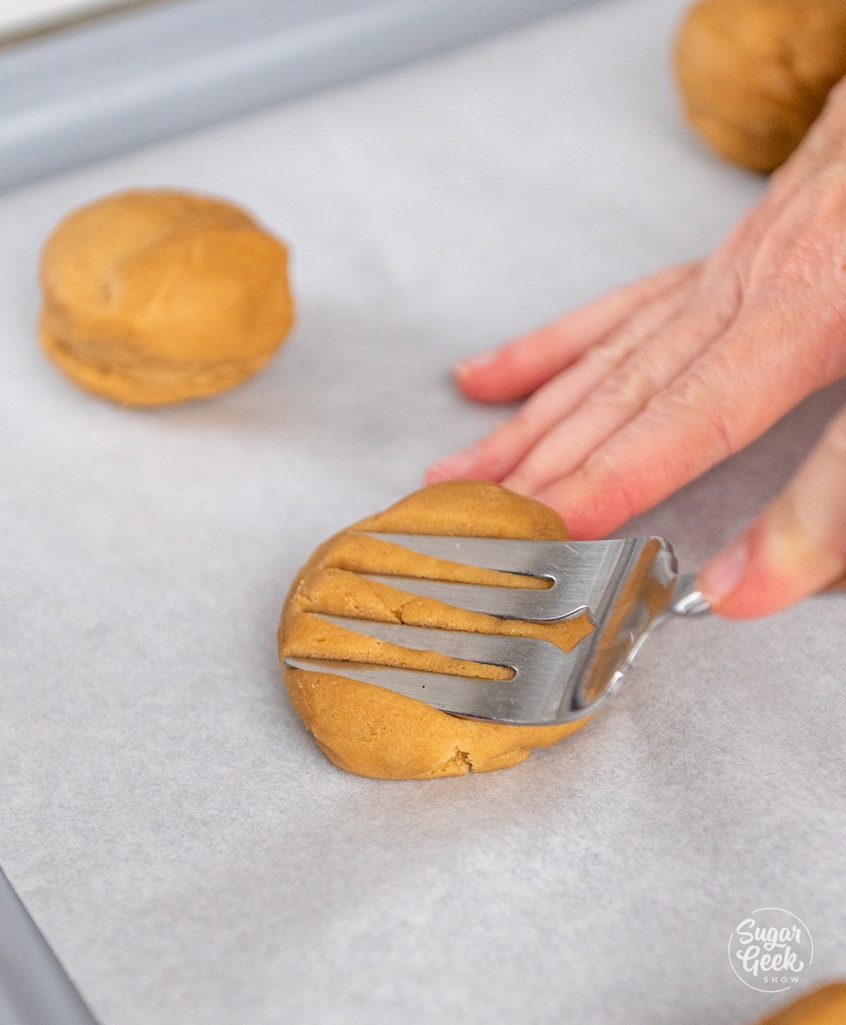 large fork pressing indents into a peanut butter cookie dough ball