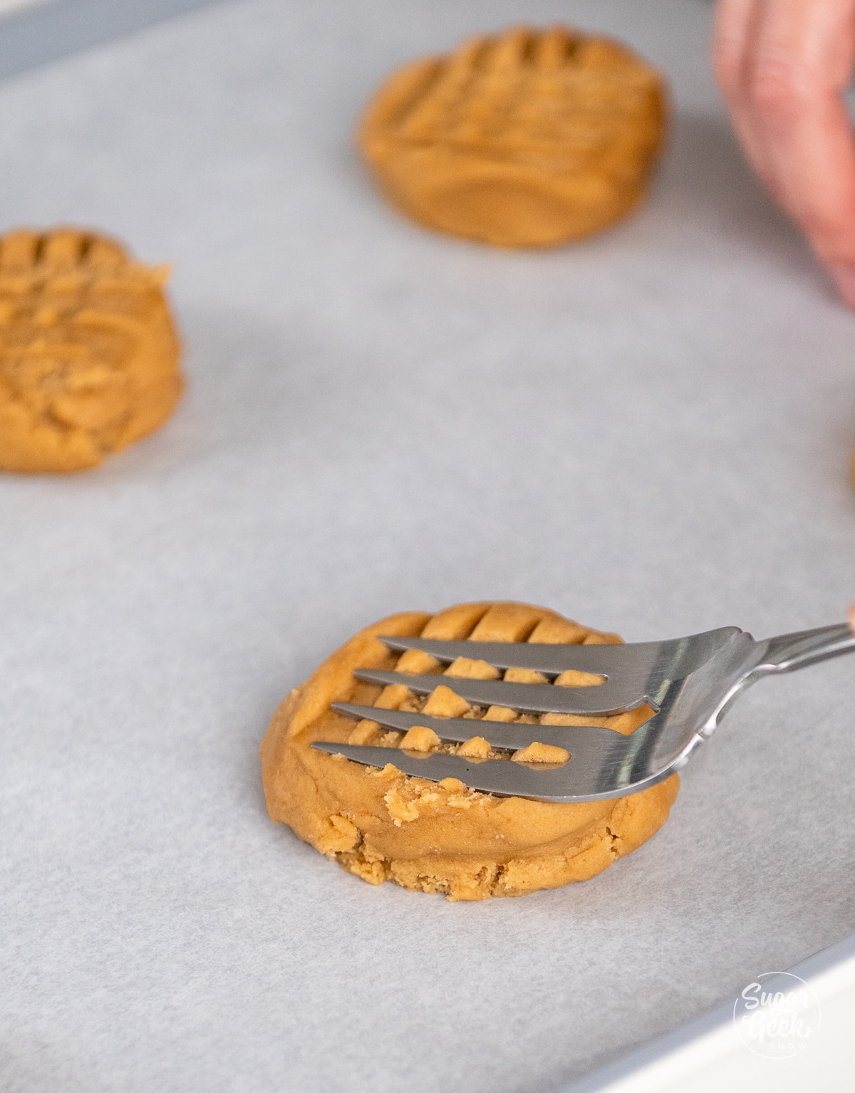 large fork pressing indents into a peanut butter cookie dough ball in the opposite direction