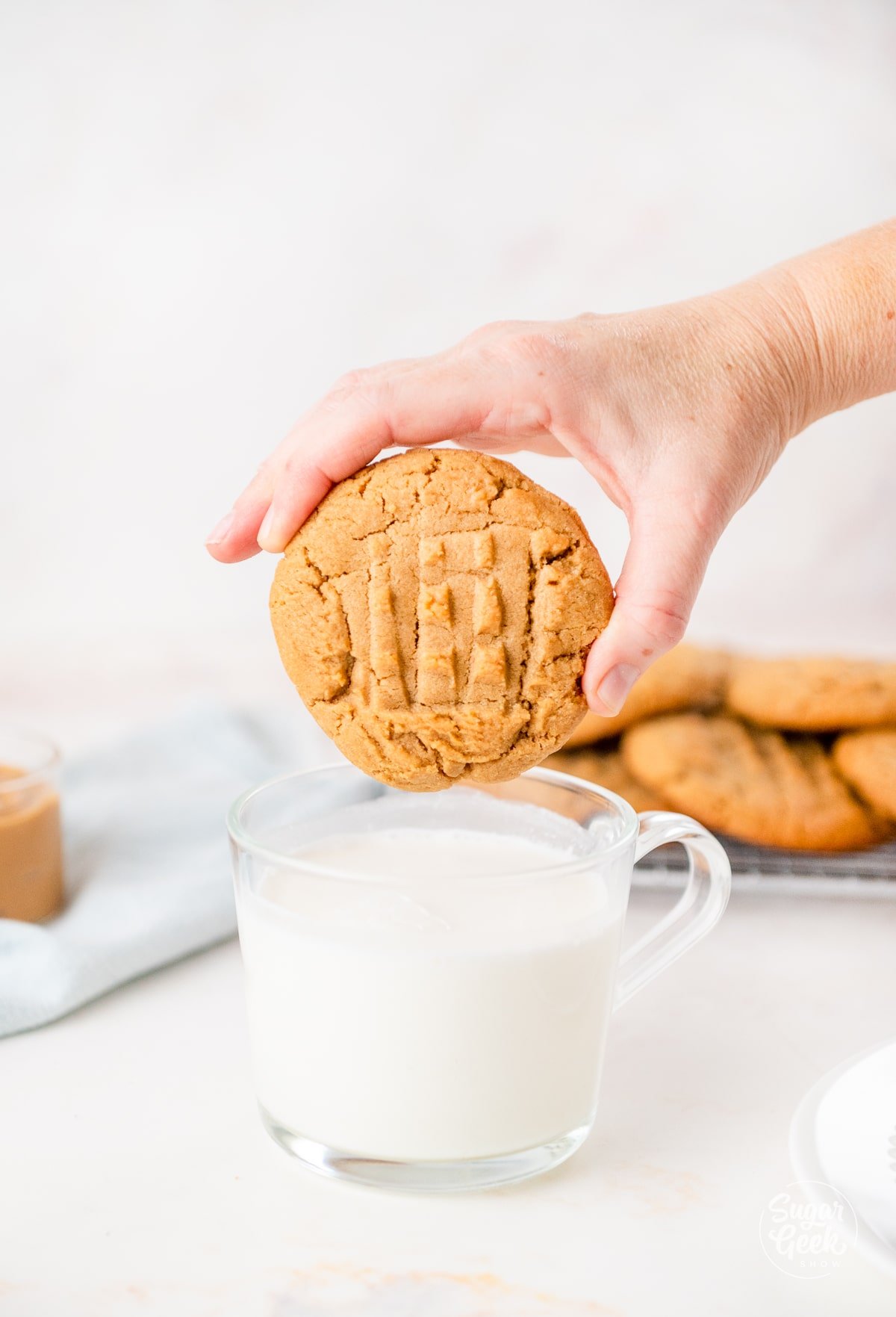 hand holding a large peanut butter cookie over a glass of milk