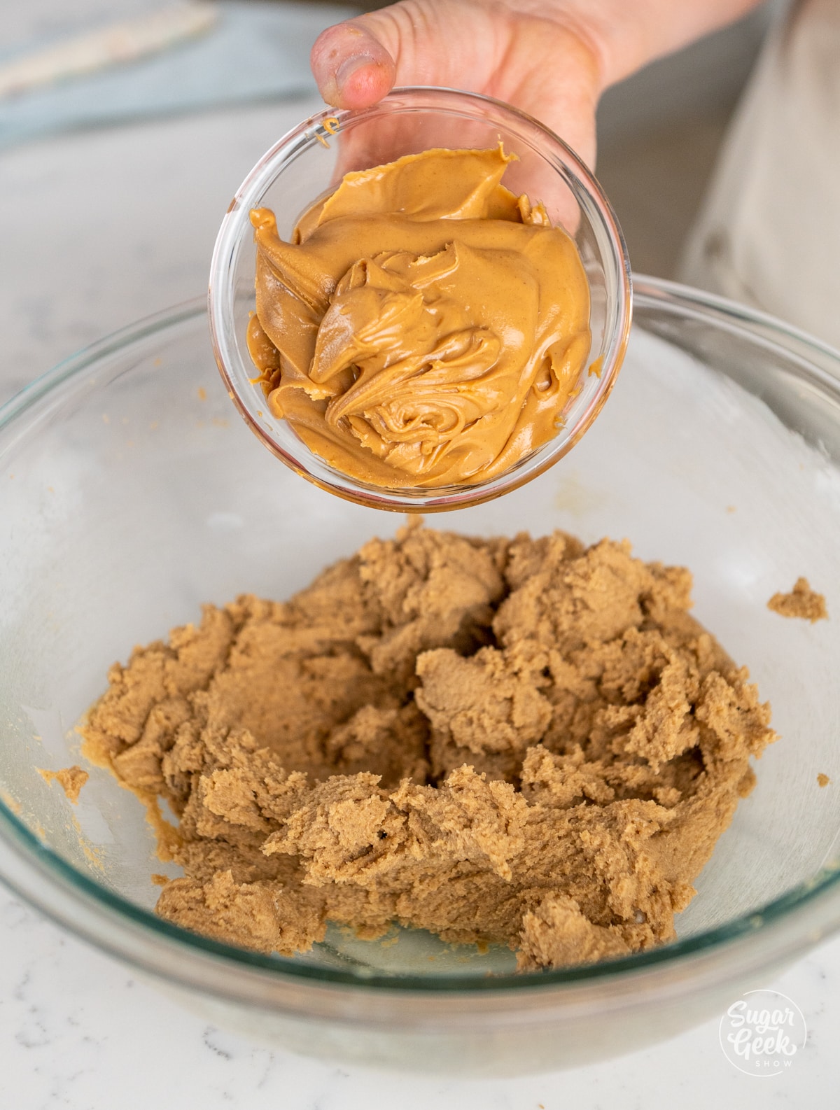 bowl of peanut butter being added into a bowl of creamed butter and sugar