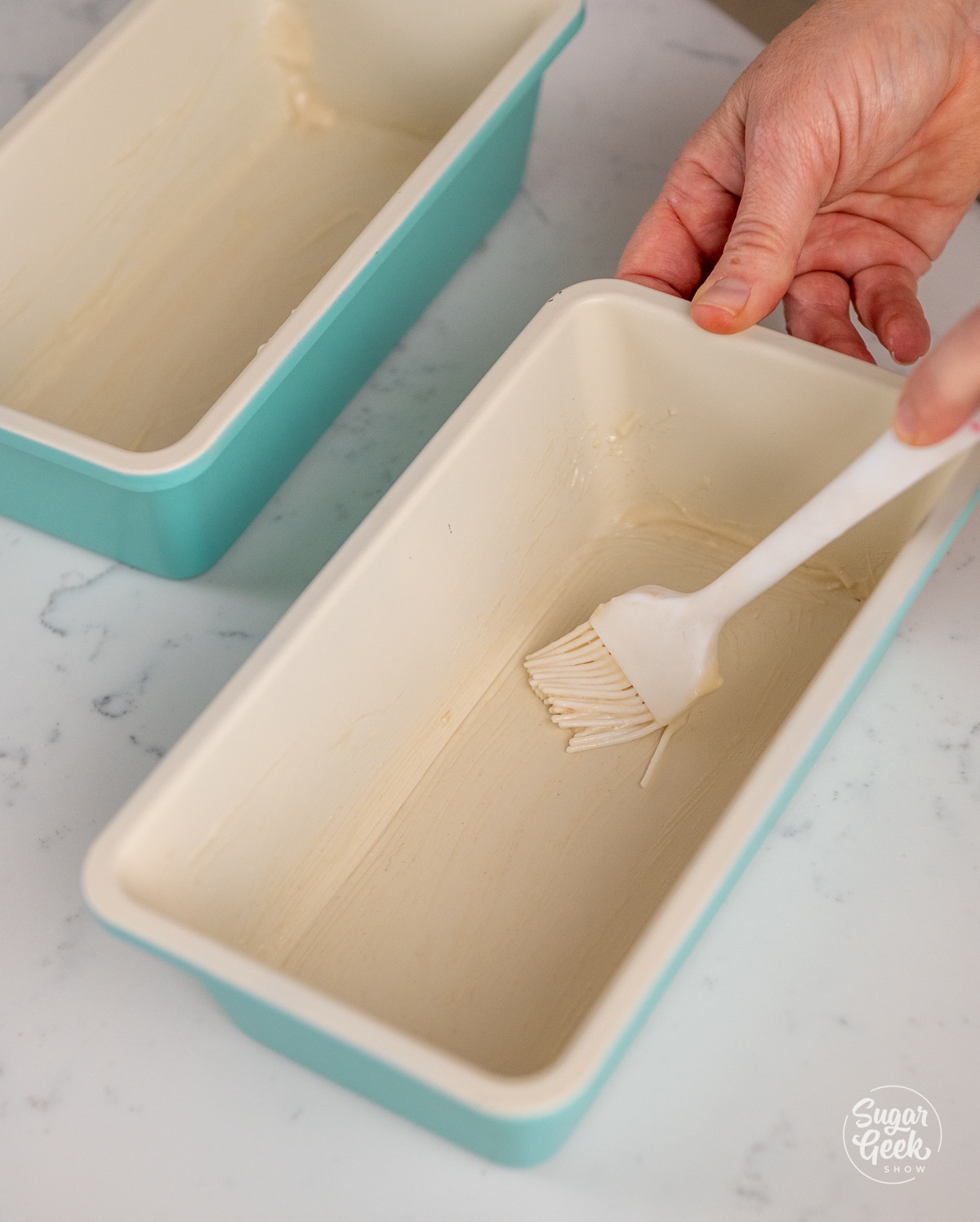 hand holding a pastry brush inside of a white loaf pan