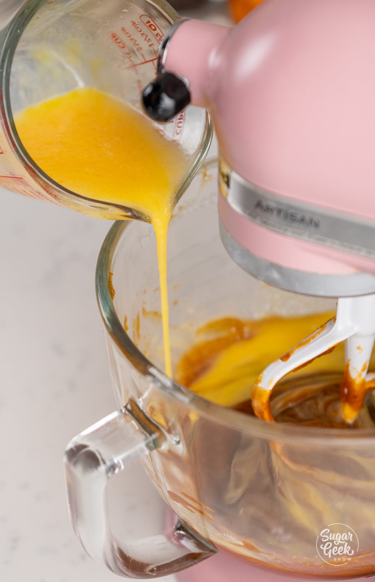 stream of egg mixture pouring into a clear glass stand mixer bowl