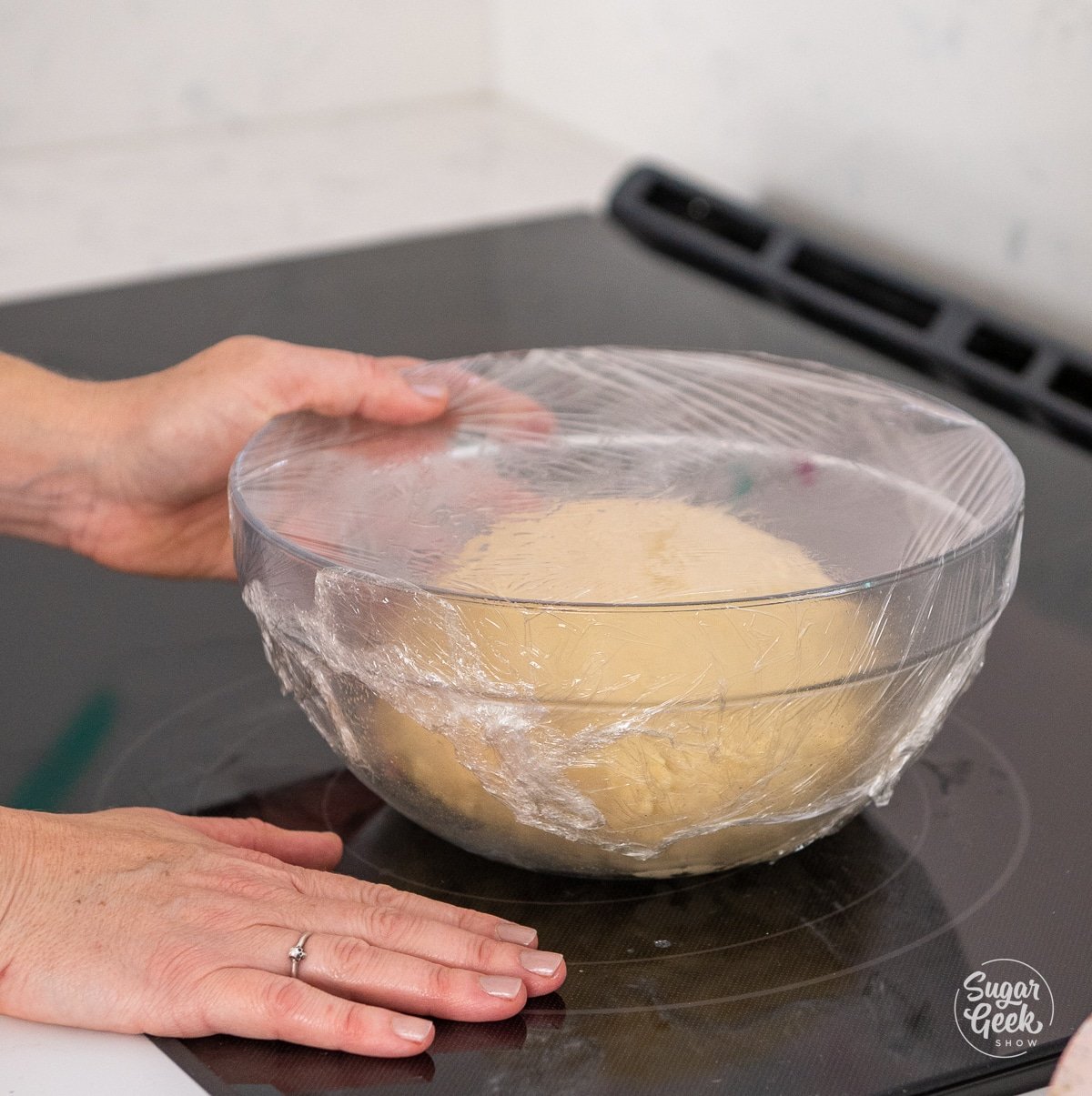 hands placing a glass bowl of dough on top of a cool stove