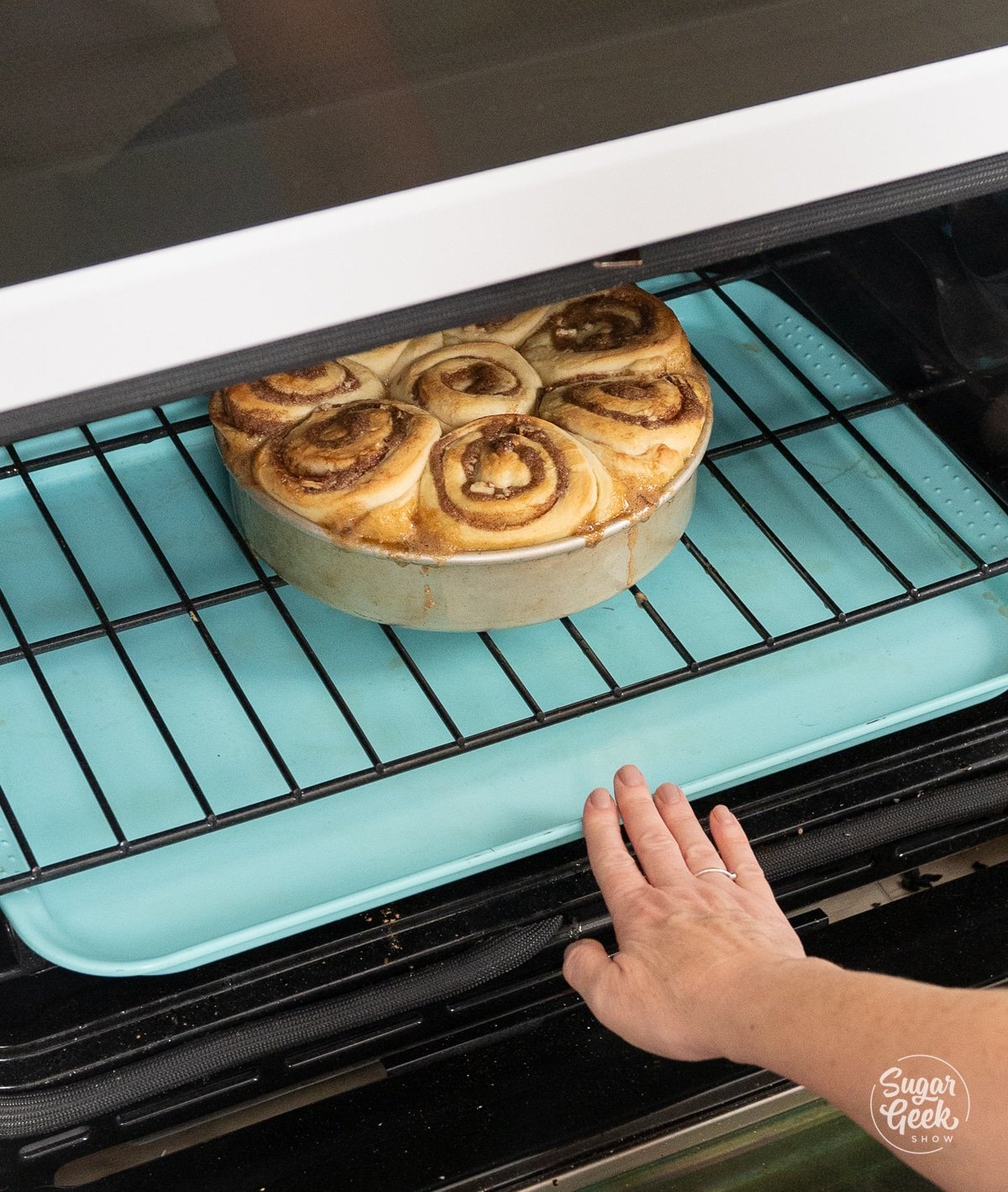 hand pushing a blue sheet pan underneath sticky buns in an oven