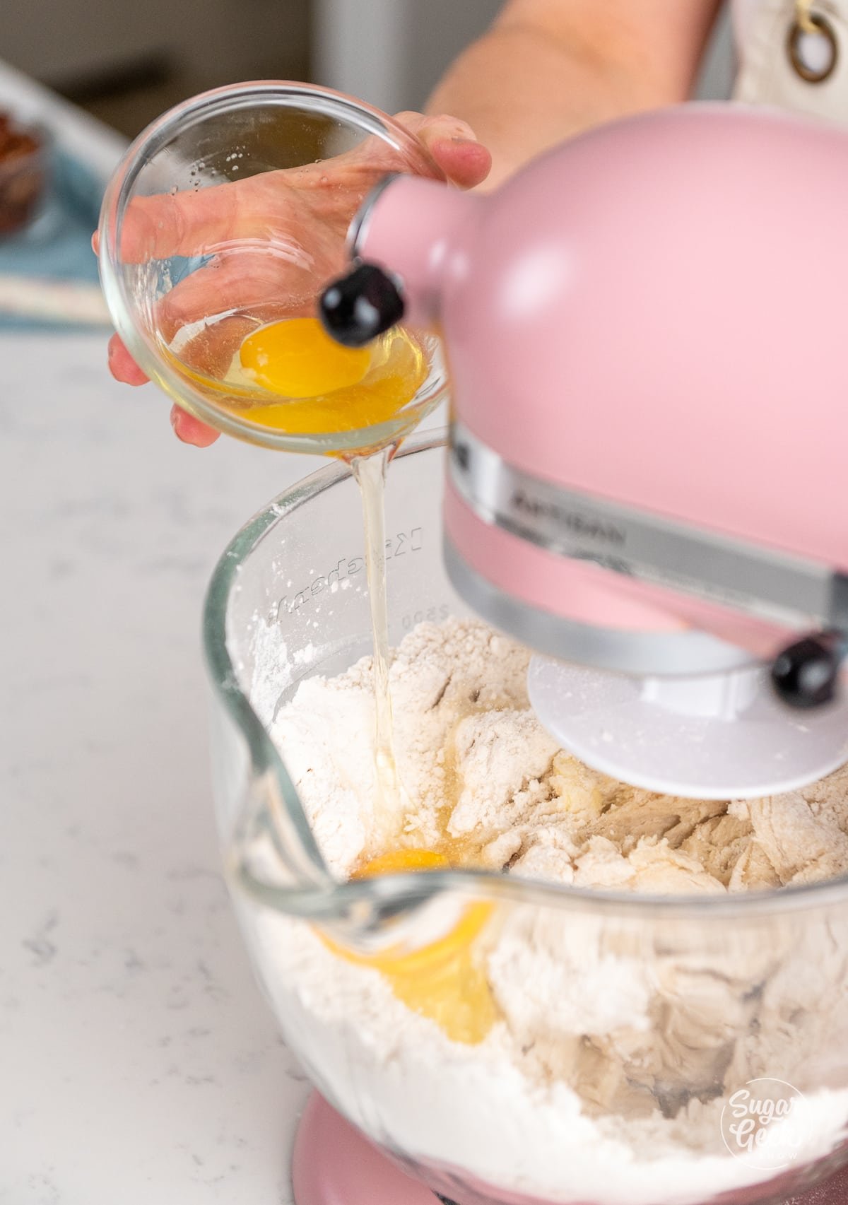hand pouring a bowl of eggs into a stand mixer bowl