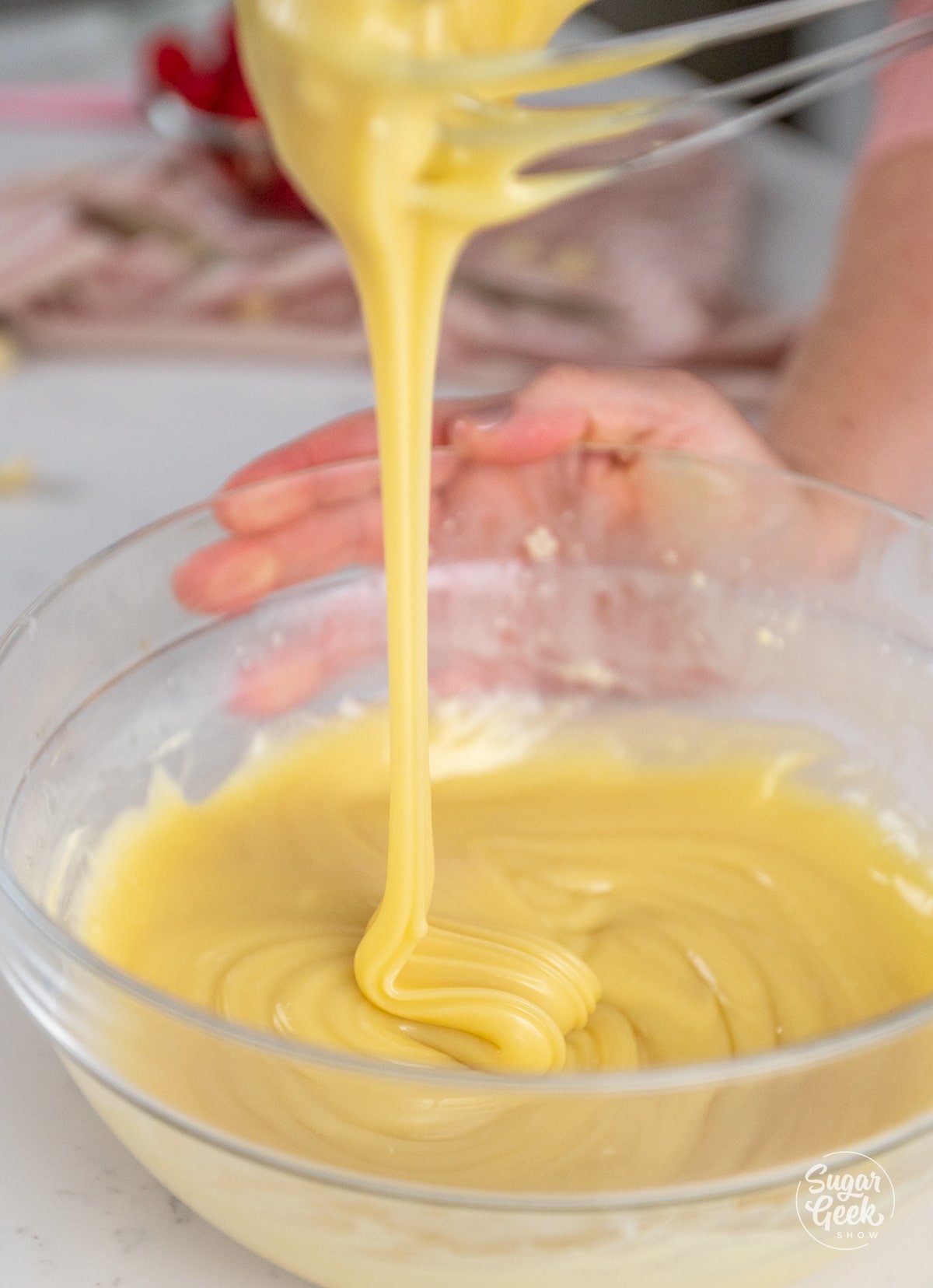 Whisk drizzling white chocolate ganache in a bowl.