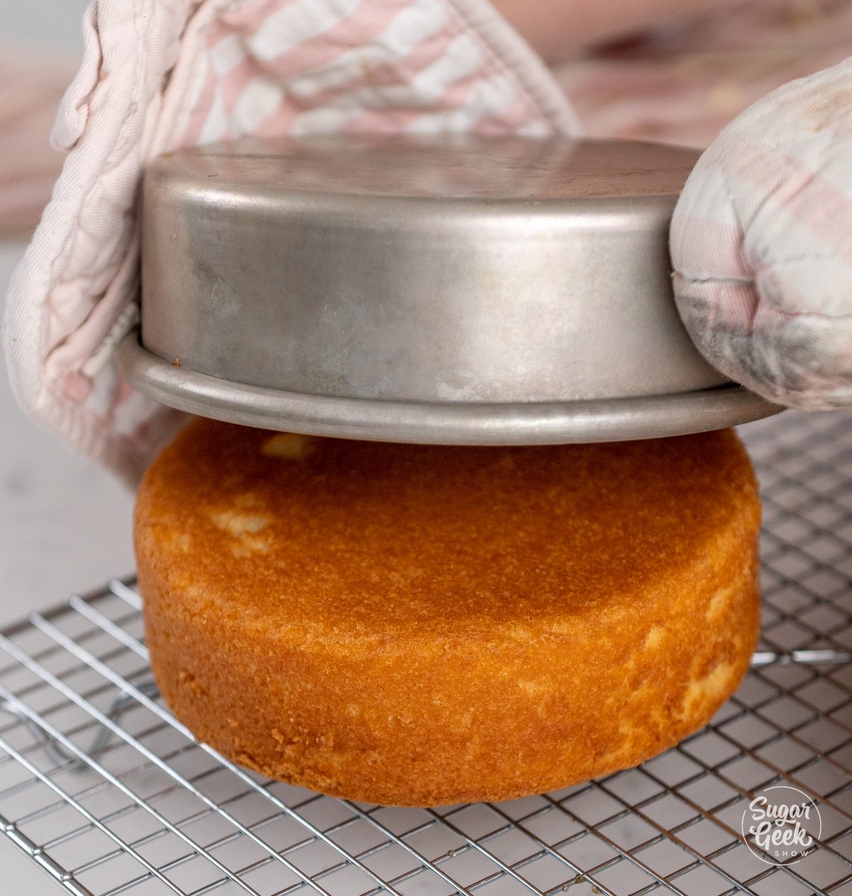 oven mitts lifting a cake pan off of a cake layer