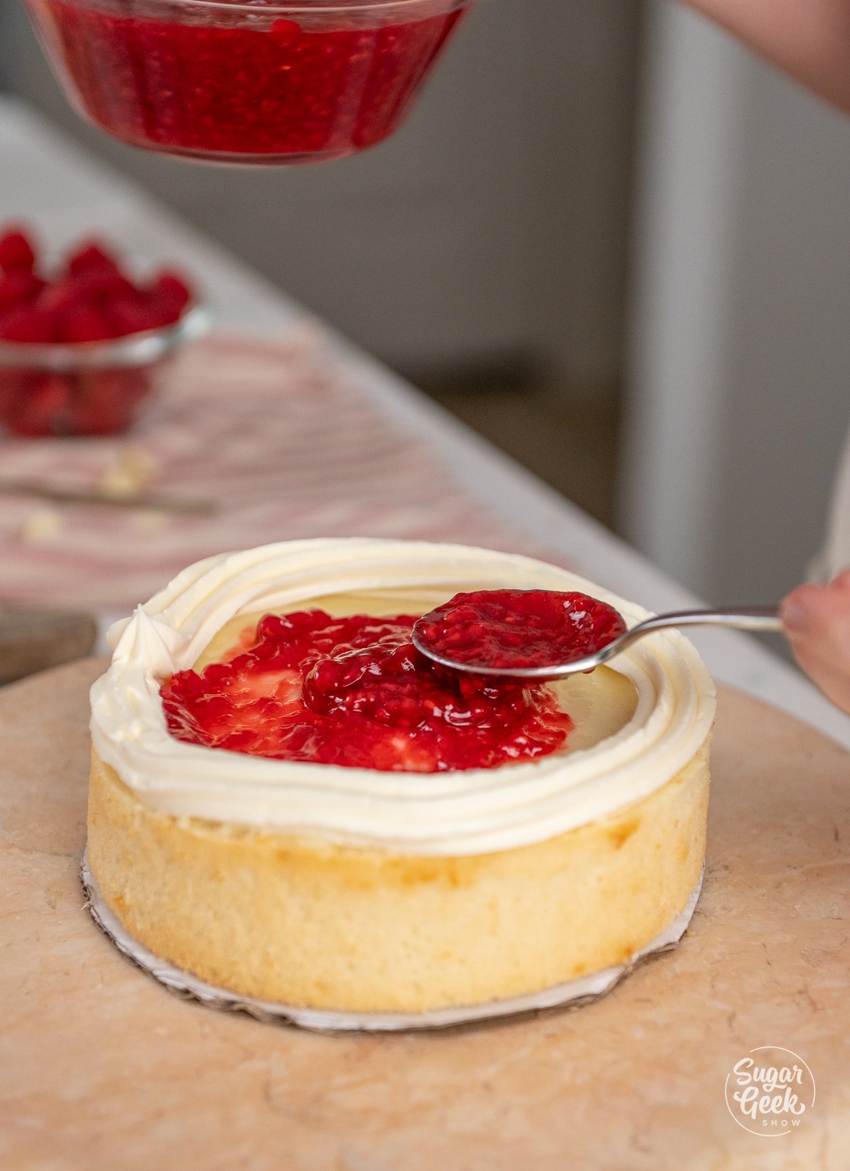 spoon spreading raspberry filling on a cake layer