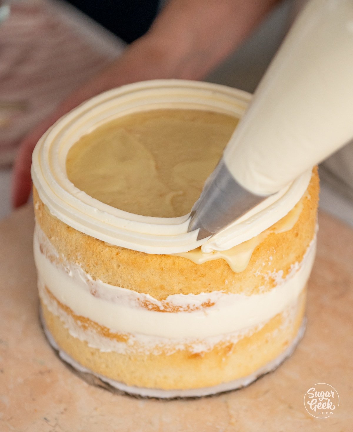 piping bag creating a dam of buttercream on a cake