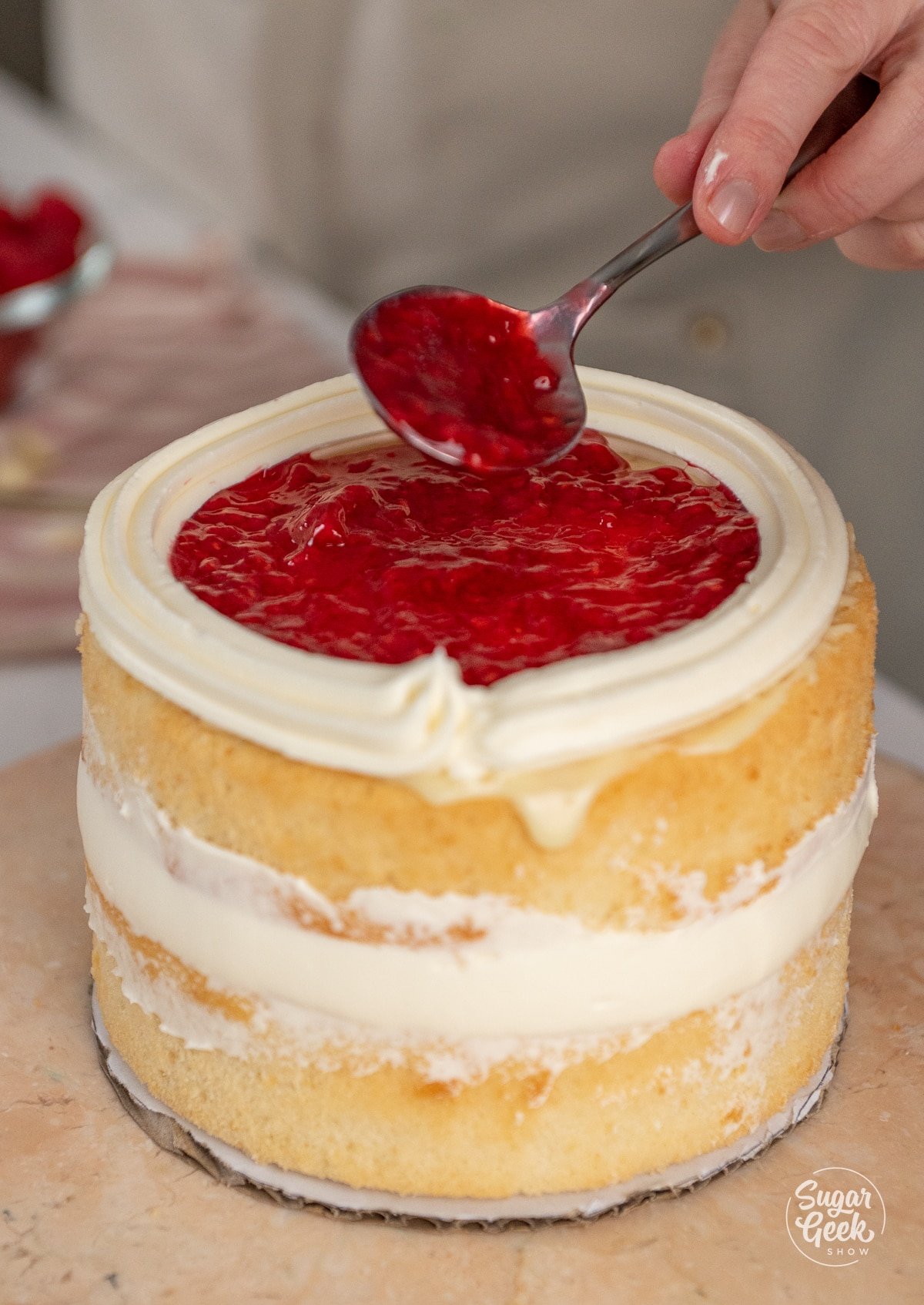 spoon spreading raspberry filling on a second cake layer.
